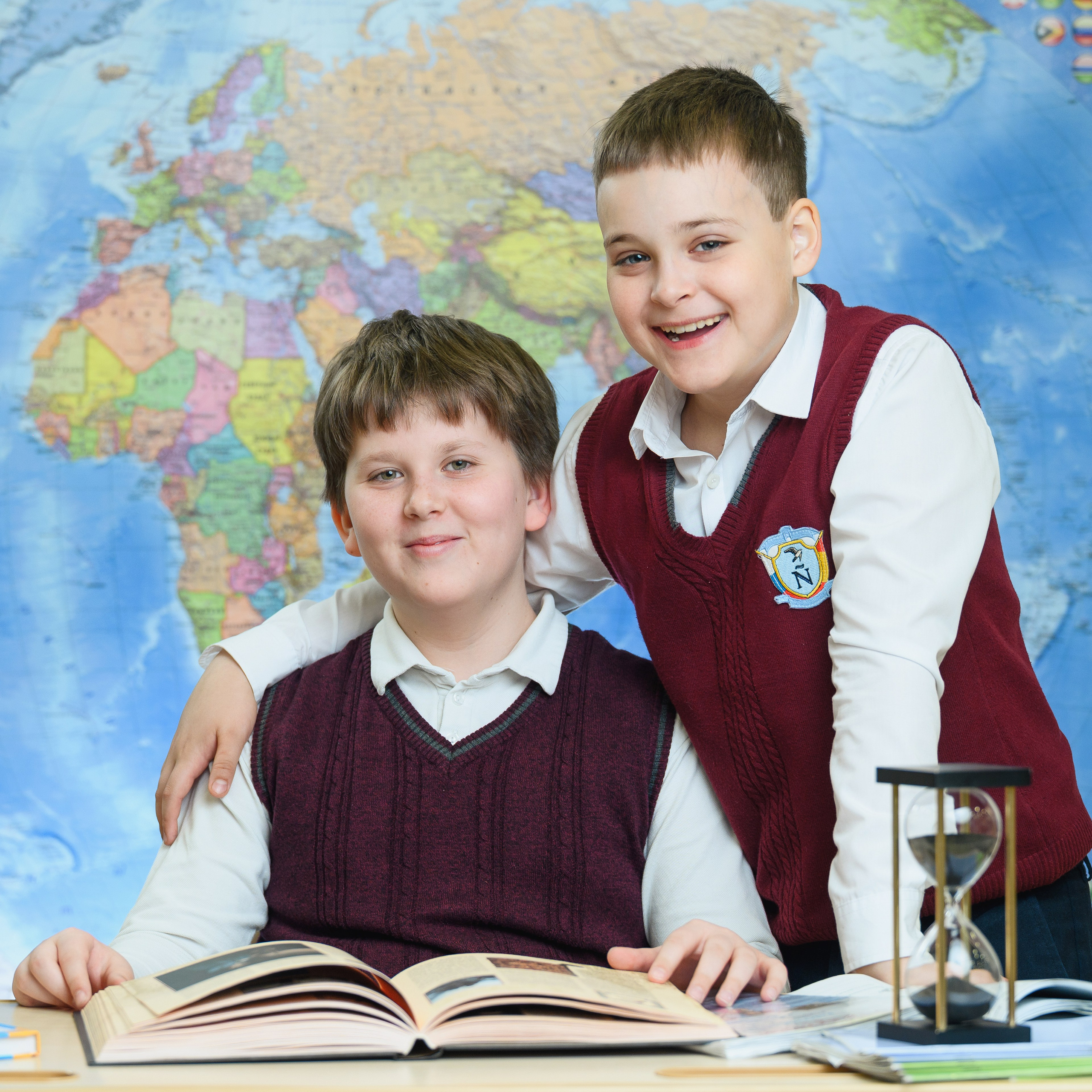 Два ученика начальной школы у карты мира в классе.