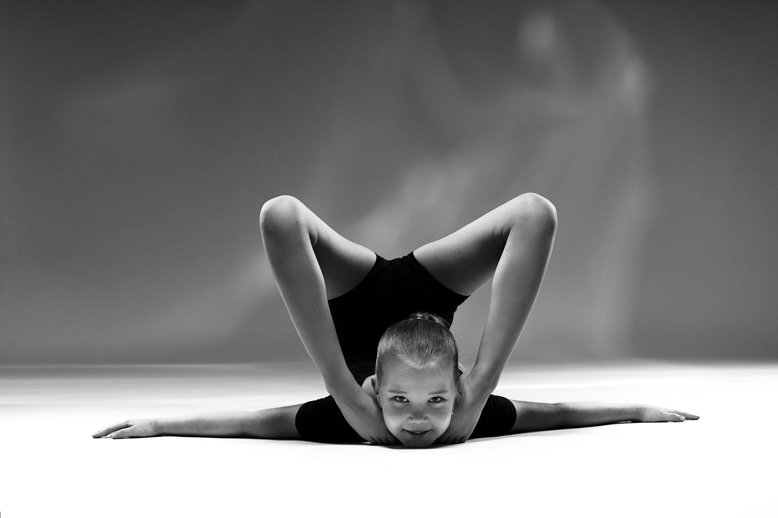 Художественное черно-белое фото гимнастки в сложной позе на гибкость. Вид спереди, симметричная композиция в стиле спорт-арт.