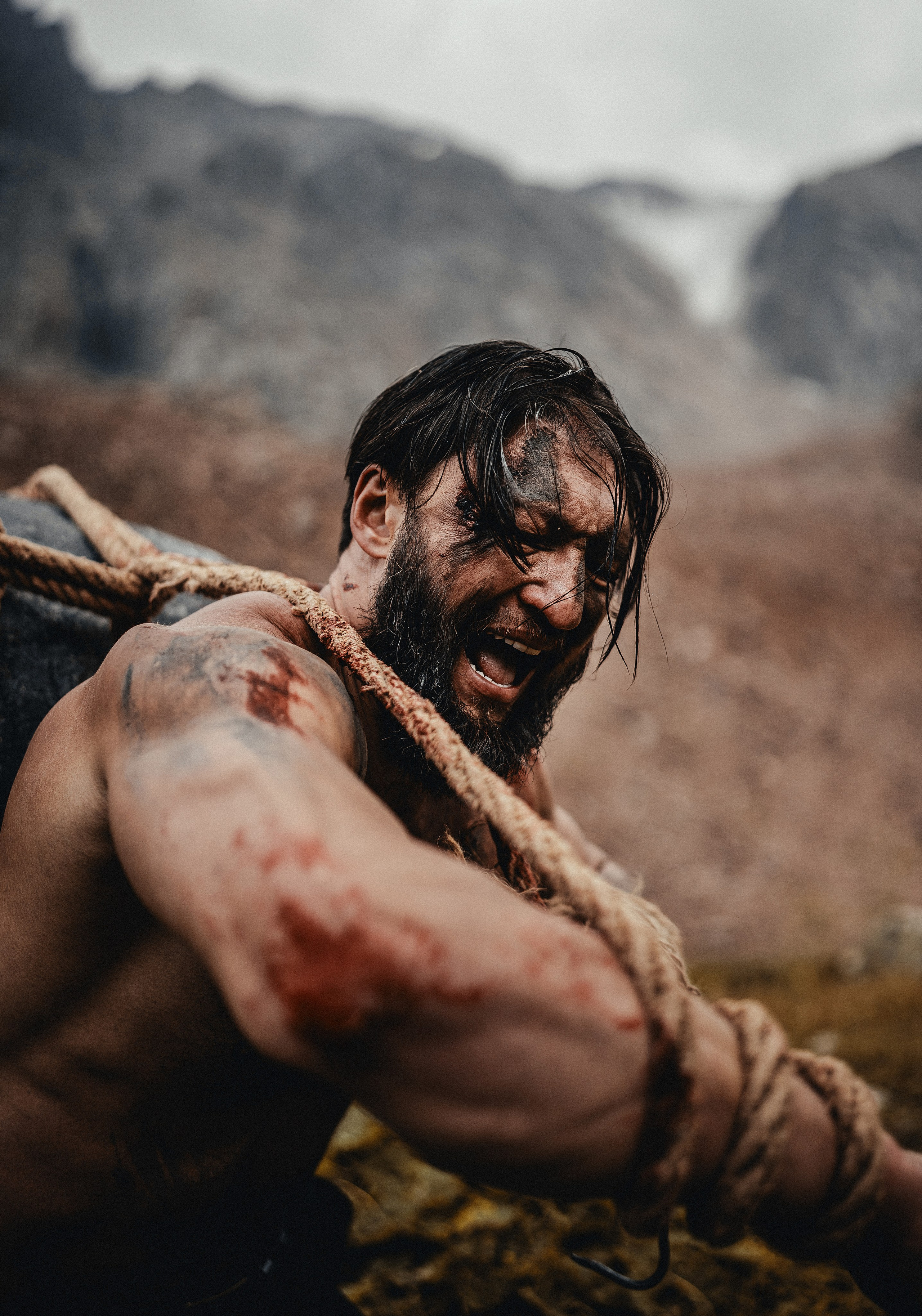 Мужчина с длинной бородой и грязным лицом тянет за собой большой камень в горах