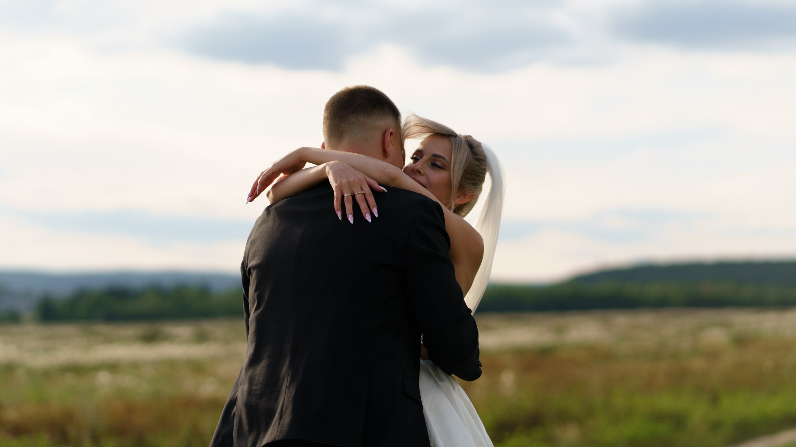 Невеста в свадебном платье с фатой обнимает жениха, выражая всю глубину своих чувств. Вокруг них — живописный пейзаж, подчёркивающий романтичность момента | фотограф для съемки первого танца Екатеринбург