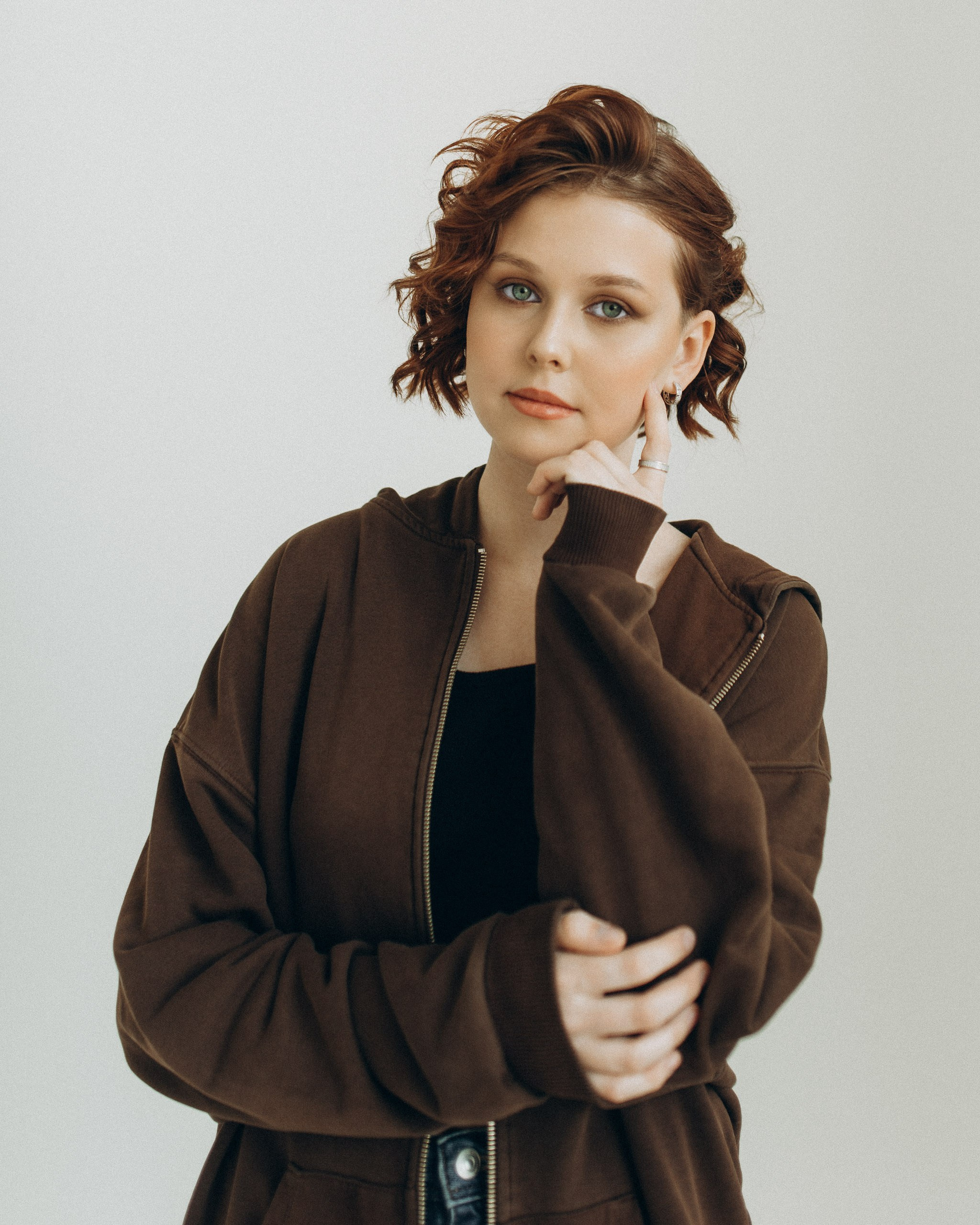 Задумчивый студийный портрет девушки с короткой рыжей стрижкой. Поясной план, рука у подбородка. Фотограф Василий Дан