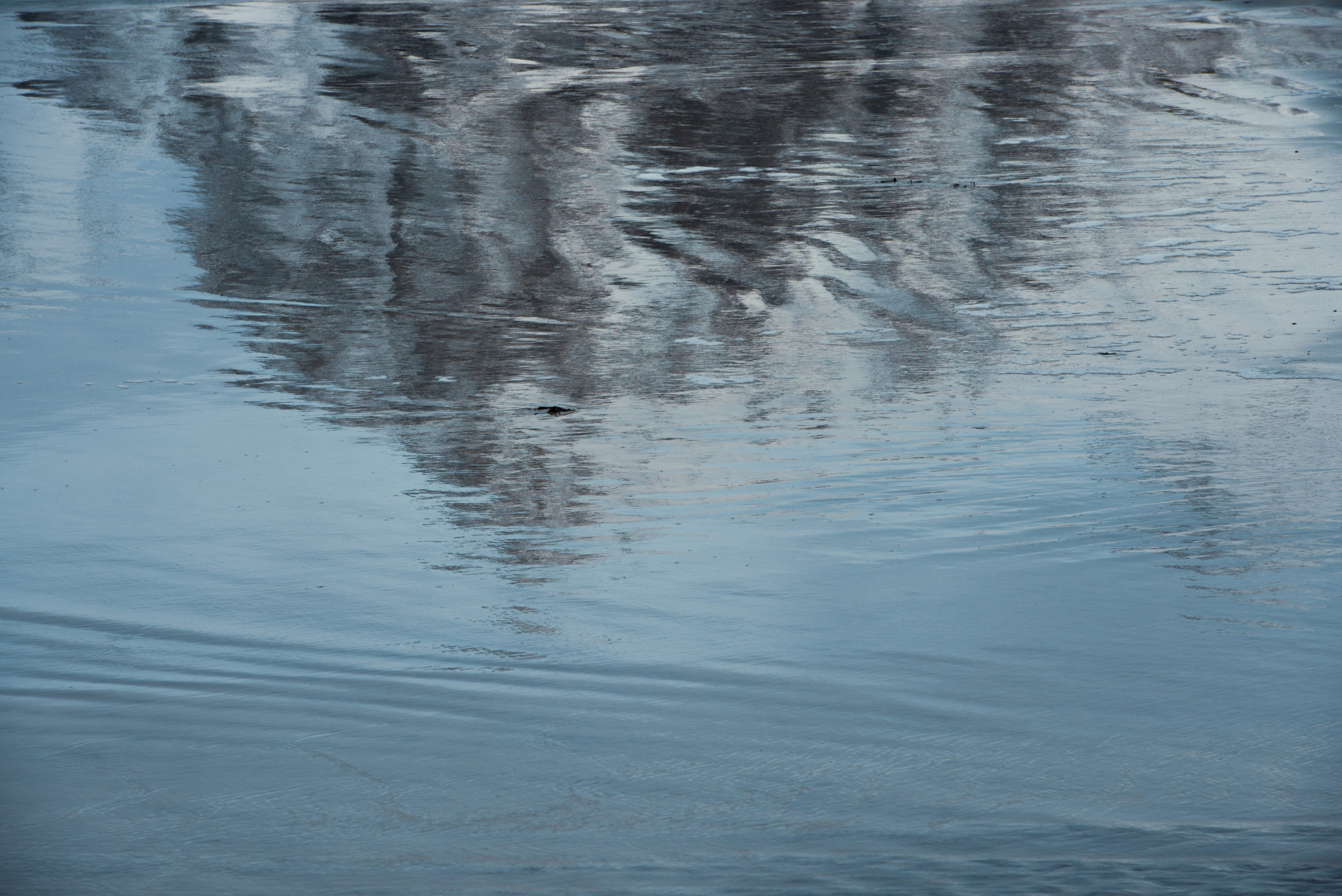 Абстрактное отражение темных гор в мелкой воде на мокром песчаном берегу с рябью.