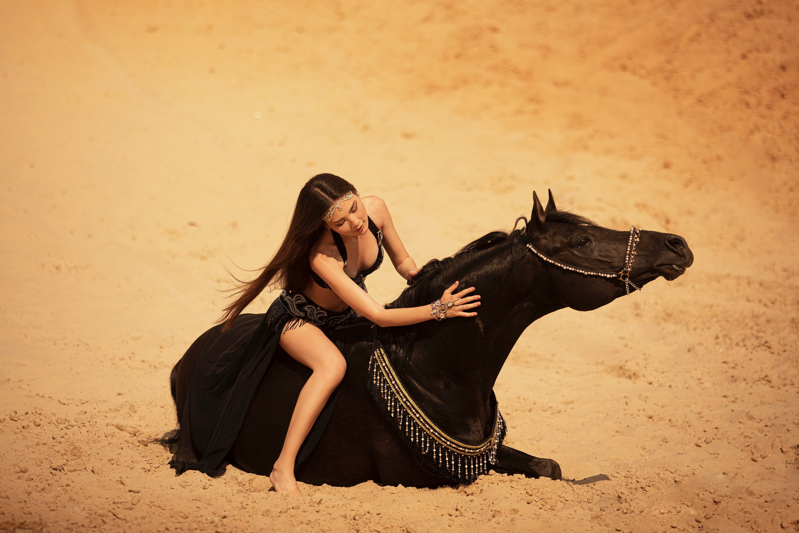 "Девушка в ярком восточном платье нежно сидит рядом с лежащей лошадью на мягкой траве. Спокойное выражение лица и расслабленная поза животного создают атмосферу умиротворения. Эта фотография идеально подходит для клиентов в Москве и области, желающих запечатлеть уникальные моменты с животными."