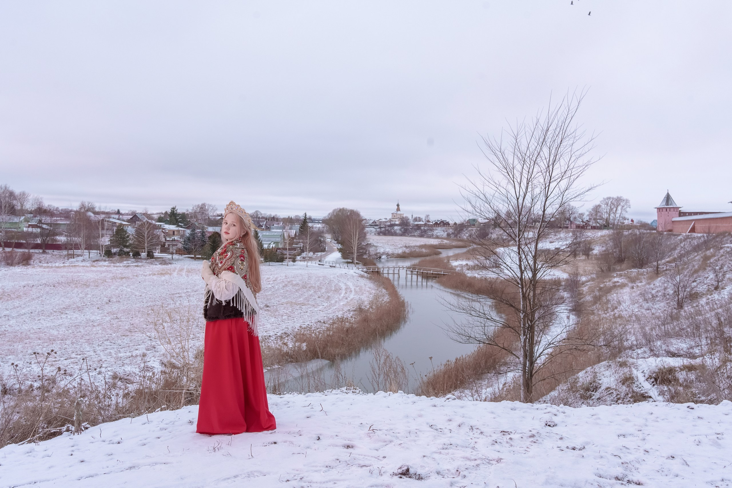 A girl in a Pavlovo Posad shawl and a red skirt on the background of a temple by the river