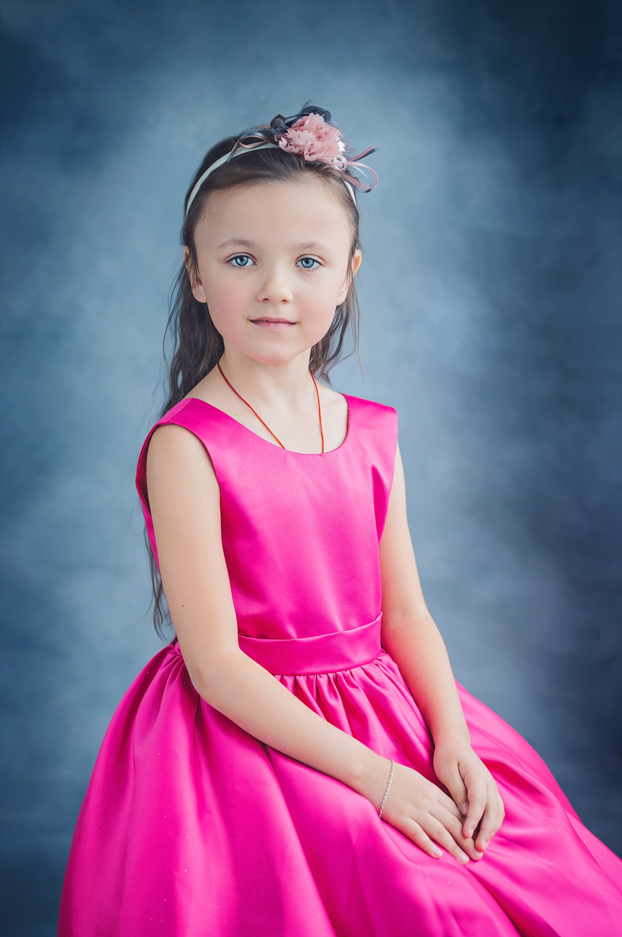 Голубоглазая девочка с темными волосами сидит на стуле в детском саду позируя для выпускного альбома