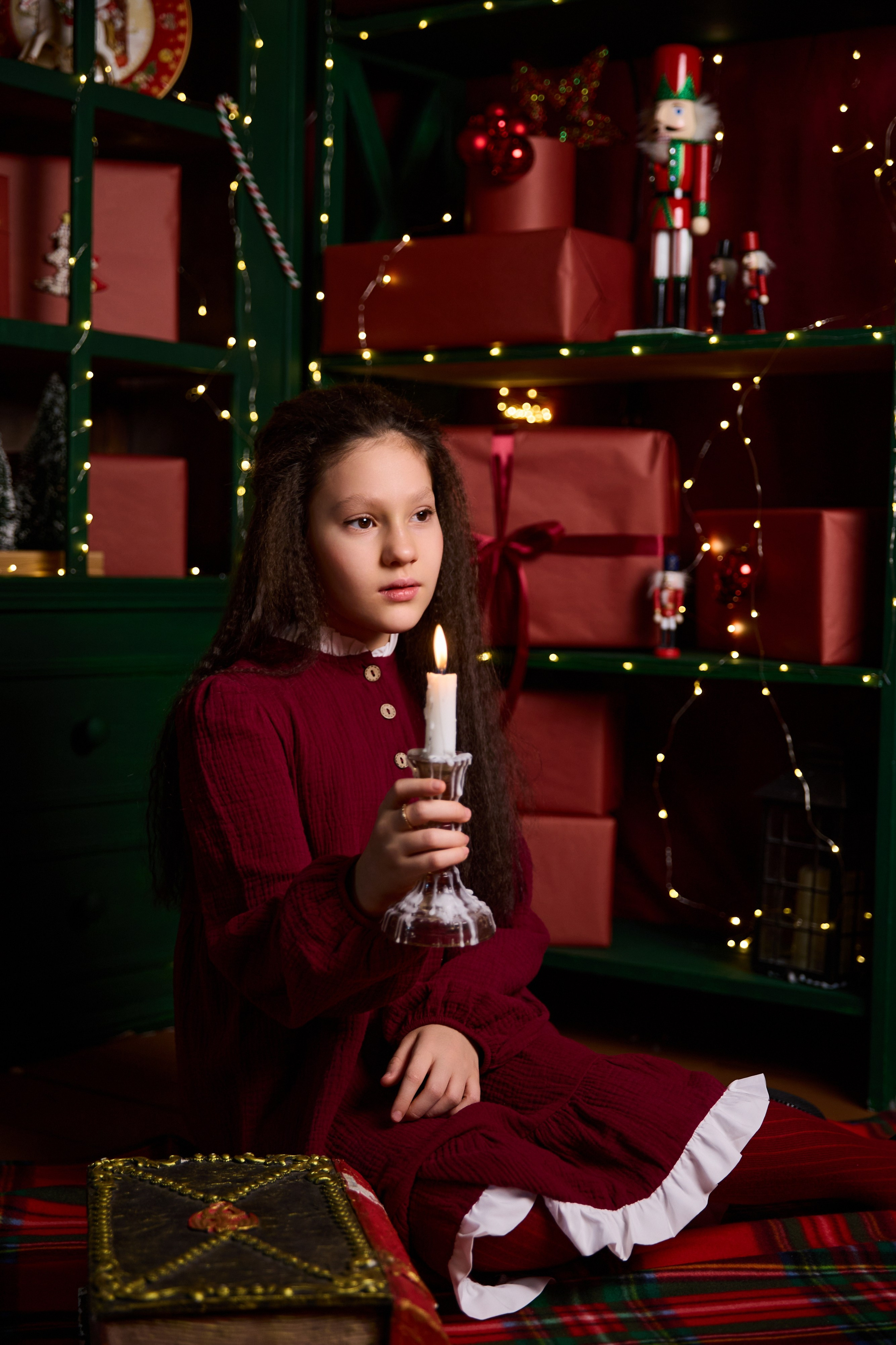 маленькая девочка в красном платье со свечой в фотостудии на новый год