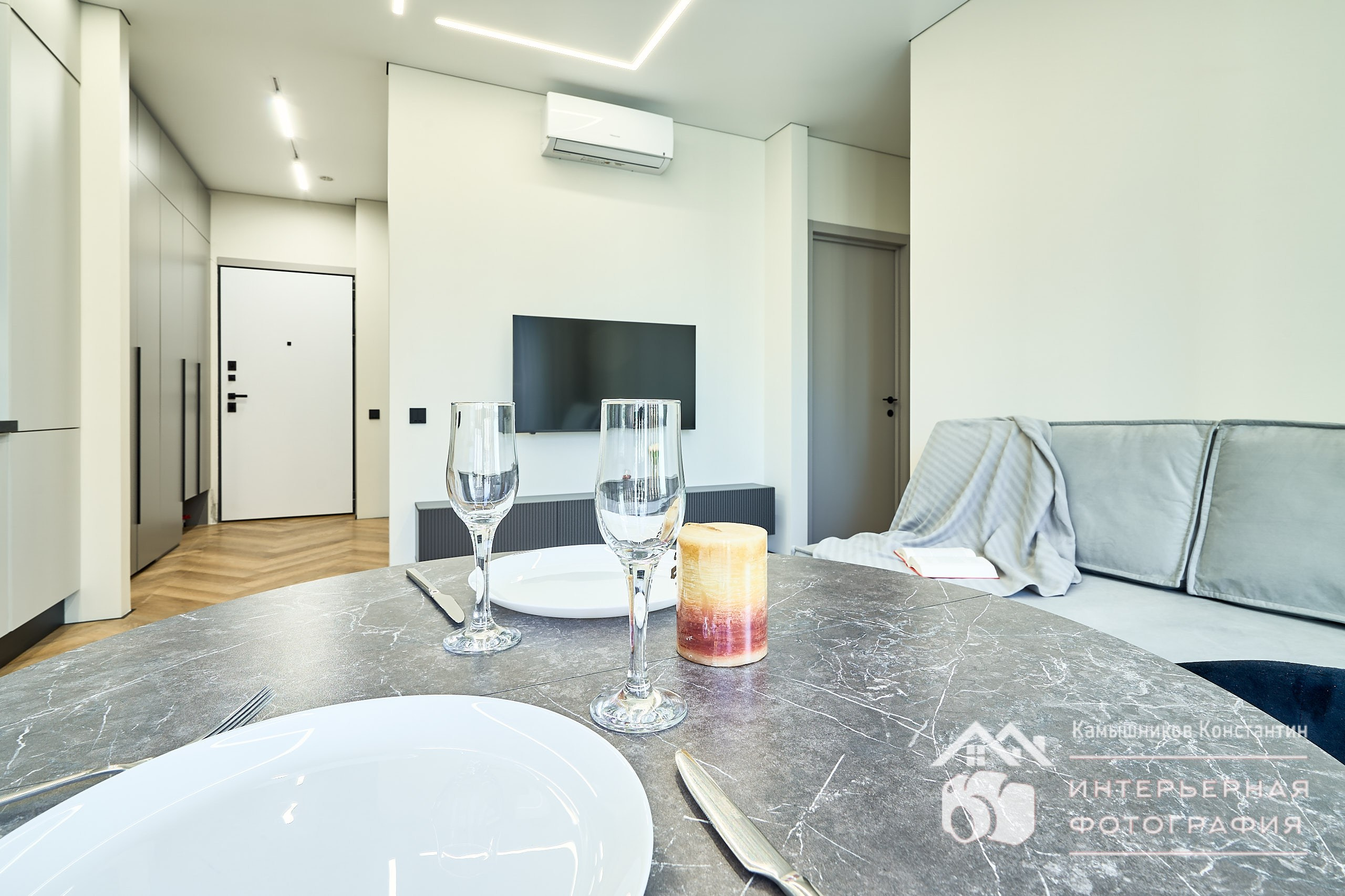 Интерьерная фотография с общим планом на гостиную и обеденным столом со столовыми приборами на первом плане в жилых апартах ЖК Метрополия, Москва