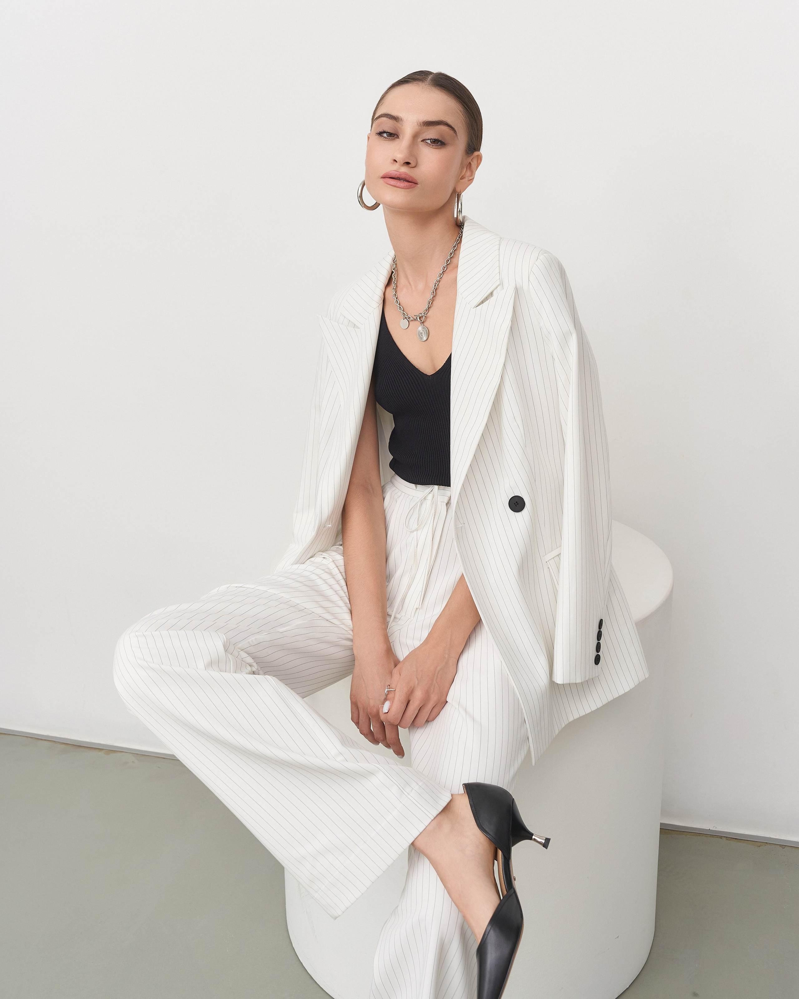 Модель в белом костюме позирует сидя на цилиндре