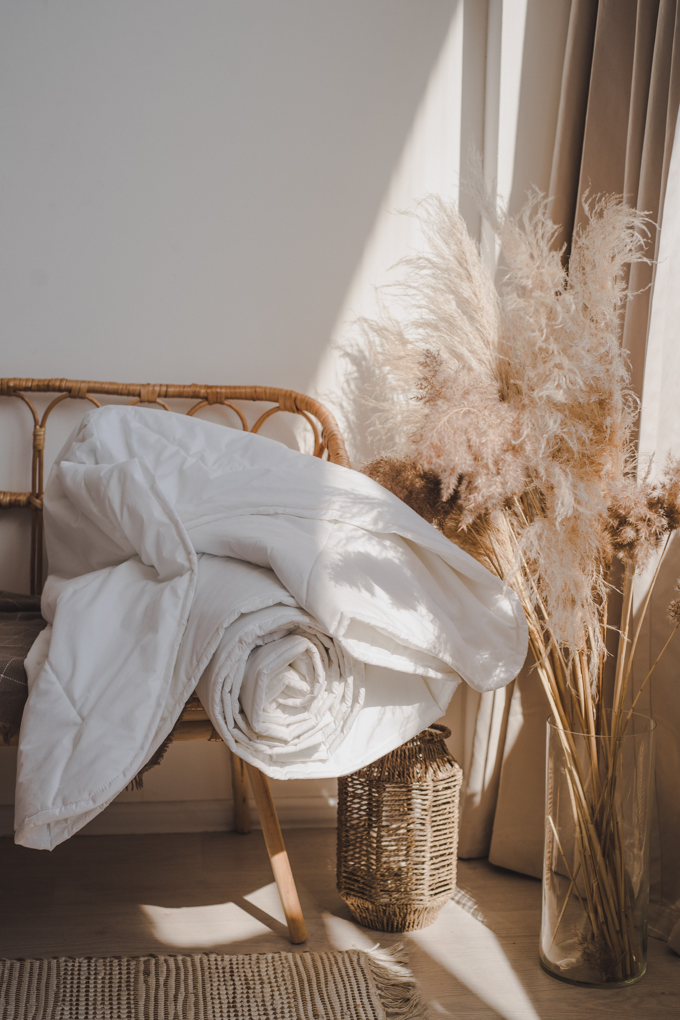 Белое одеяло свернуто лежит на плетеном стуле