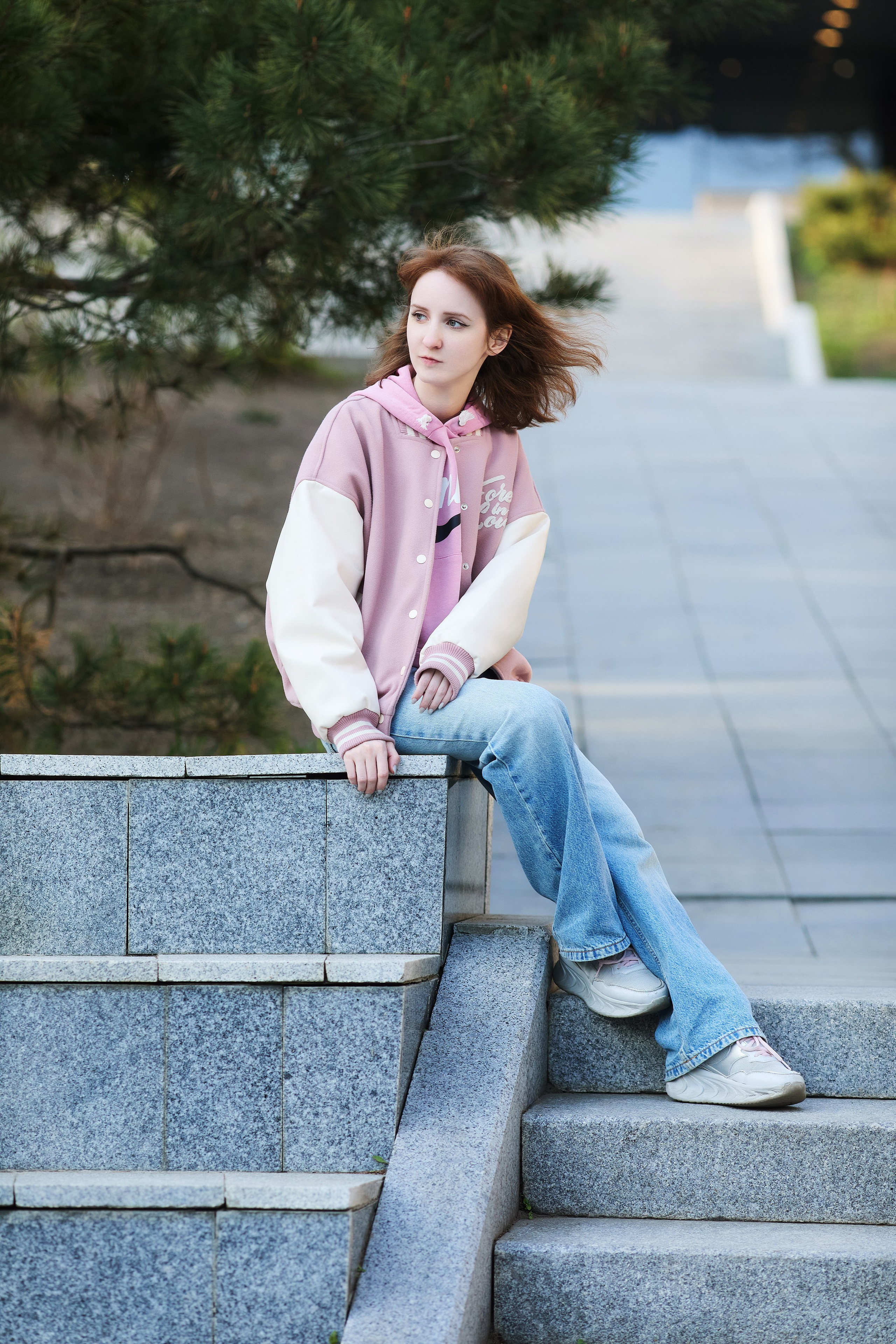 Идея позы для фото на улице с молодой девушкой, сидящей на краю бетонного ограждения в центре города Владивостока