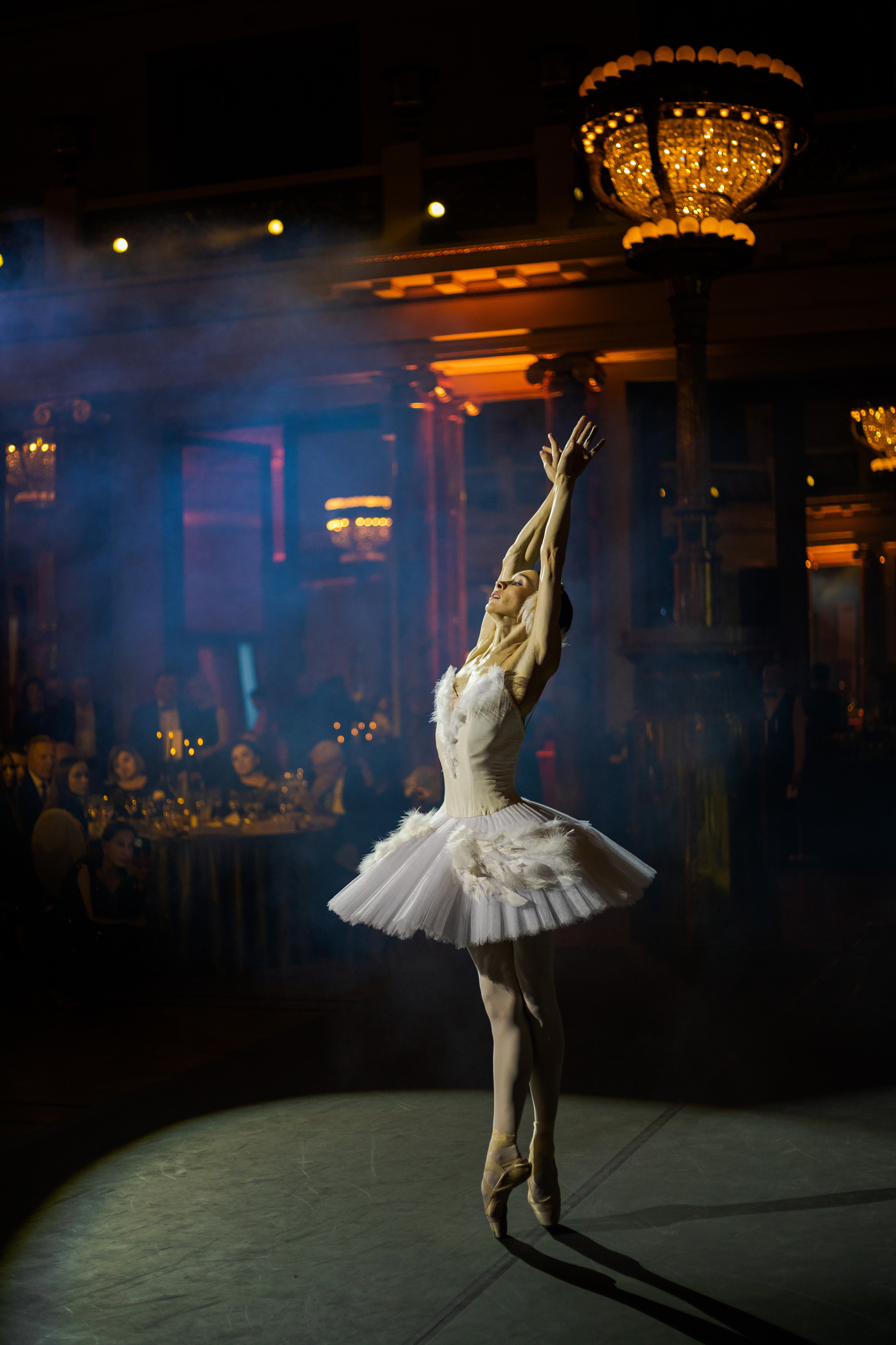 Фотосъёмка новогоднего вечера в отеле 'Метрополь' в Москве. На фотографии — элегантно украшенный банкетный зал, наполненный атмосферой праздника. Зал украшен яркими новогодними гирляндами, сверкающими огоньками, и роскошными цветами. Гостям, одетым в вечерние наряды, подают шампанское. В центре — большой новогодний стол с праздничными угощениями, в фоновом освещении виден величественный интерьер отеля, создающий атмосферу торжества и роскоши