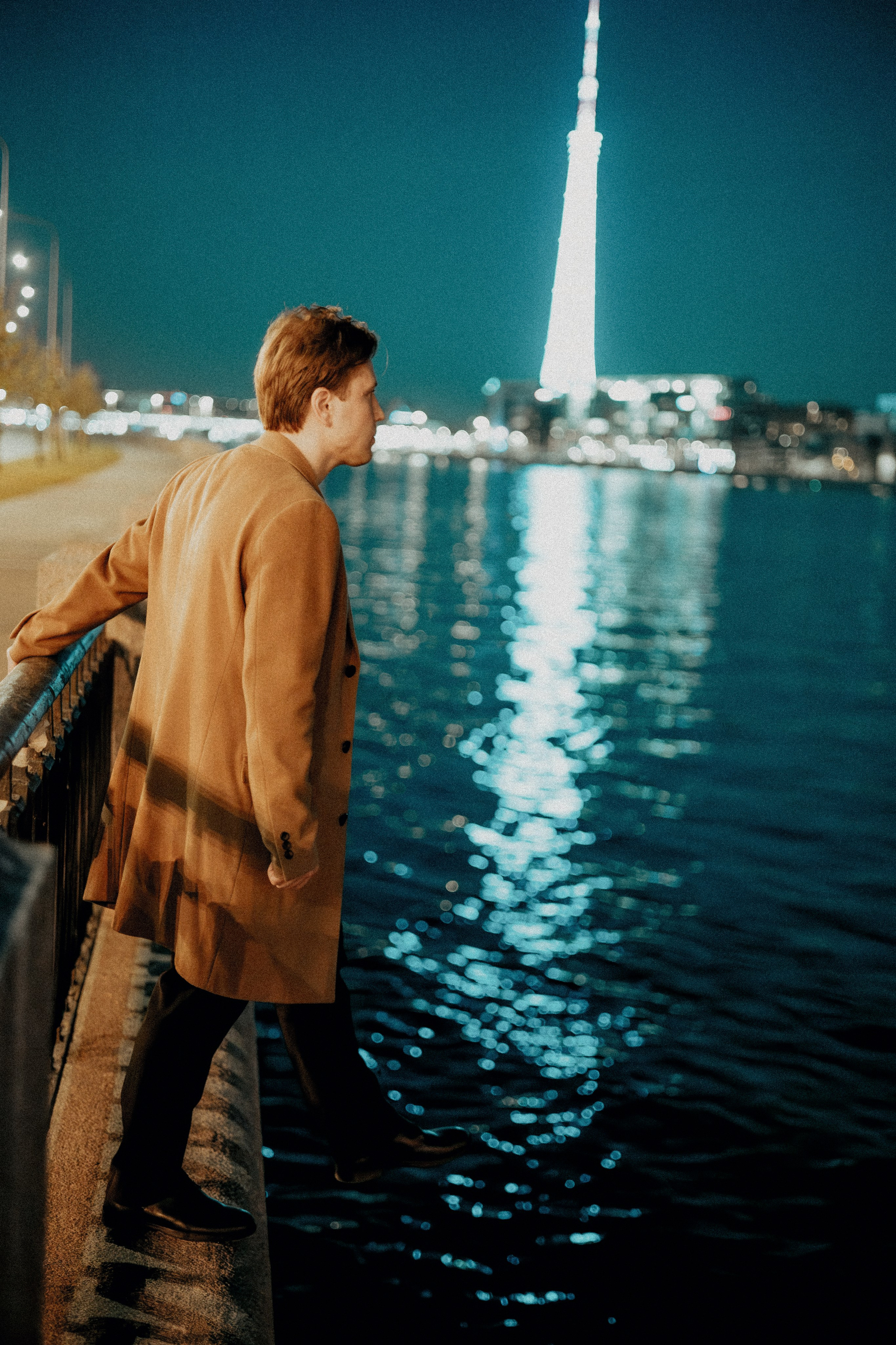 Молодой человек в пальто хочет шагнуть в воду ночью.