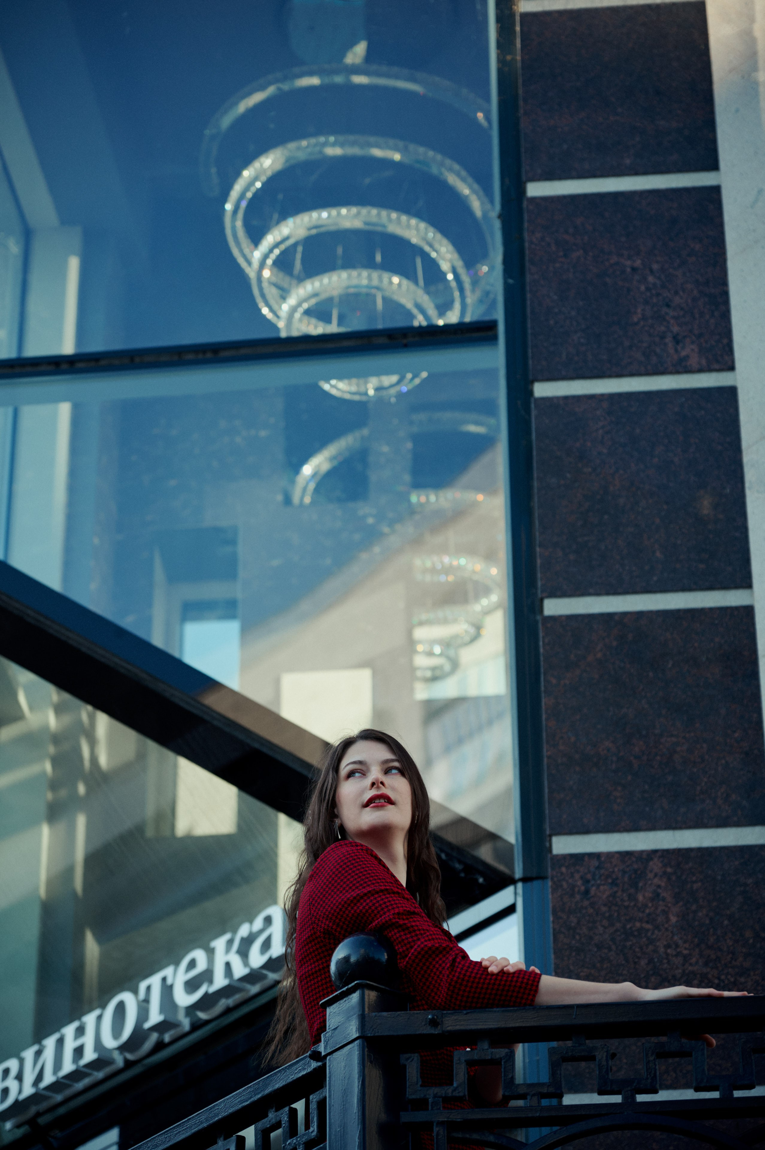 Архитектурная деталь в городе — стеклянный фасад с люстрой; в нижней части кадра — женщина на фоне вывески.