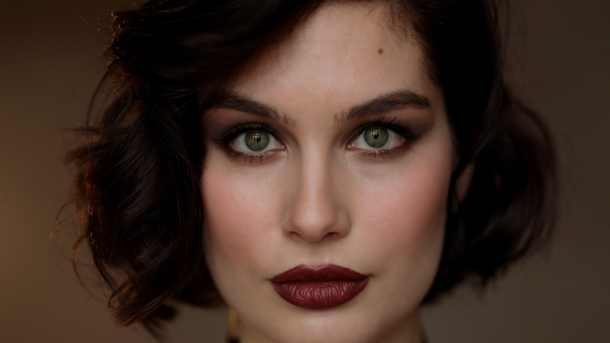 Портрет девушки в анфас, крупный план, глаза ярко-зелёного цвета, тёмные волосы и губы накрашены ярко-терракотовой помадой, волосы до плеч, уложены в ретро укладку