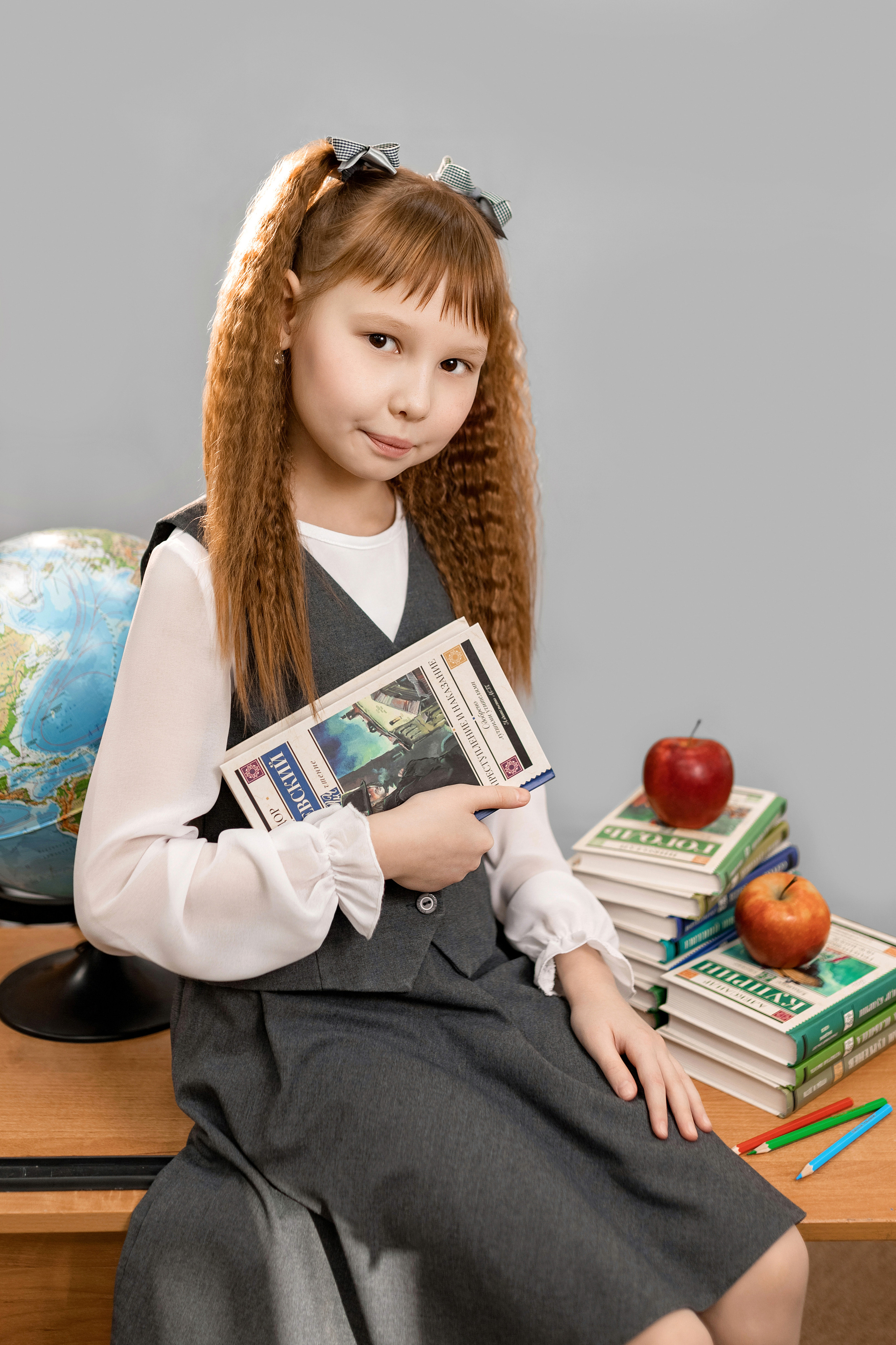 девочка в школьной форме сидит на парте с книгой и глобусом