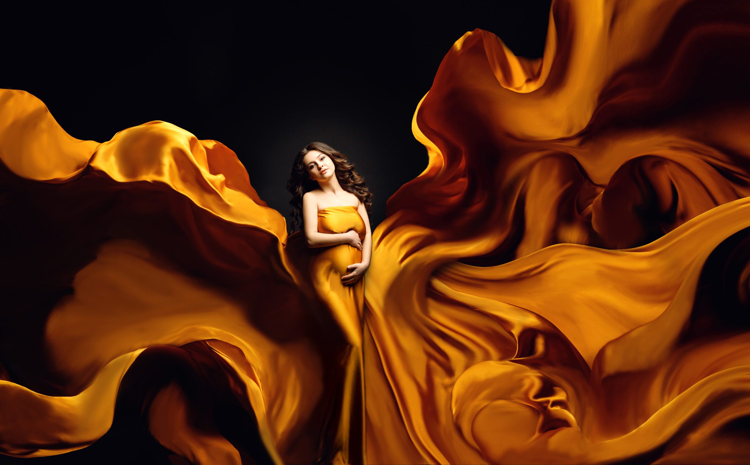 Фото беременности в Москве в летящих тканях на черном фоне.