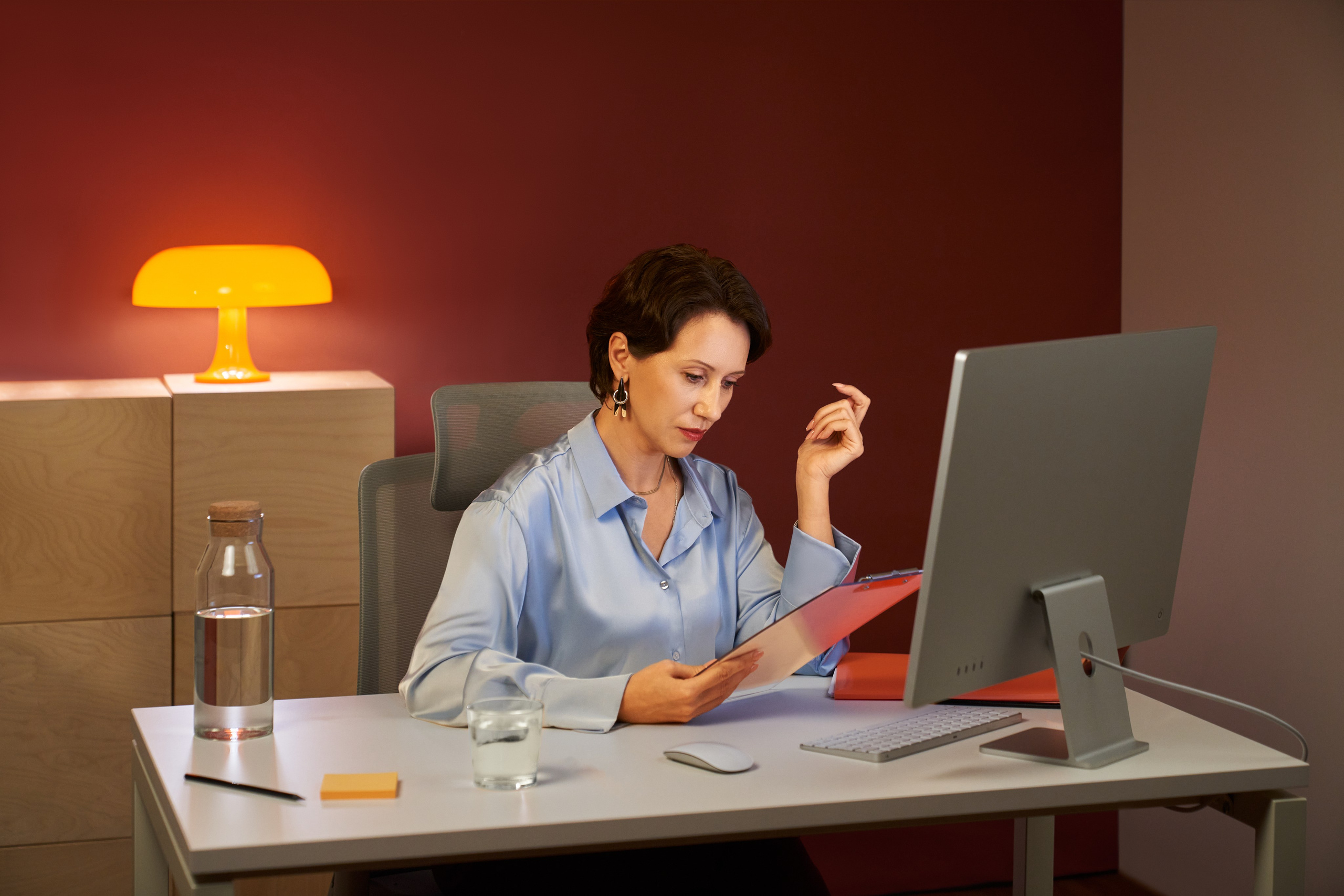 Женщина в голубой рубашке работает за компьютером и изучает документы в современном офисе