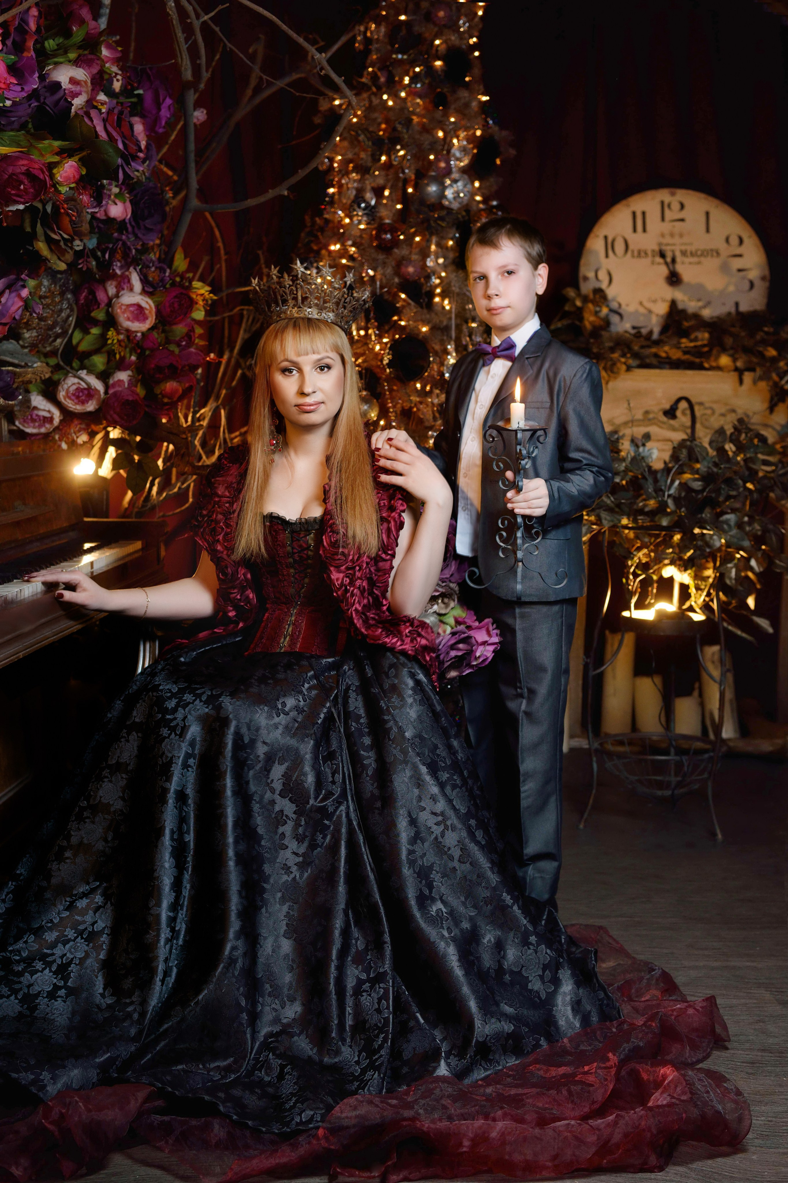 Мама в костюме королевы сидит на троне, рядом стоит сын, на фоне новогодняя елка