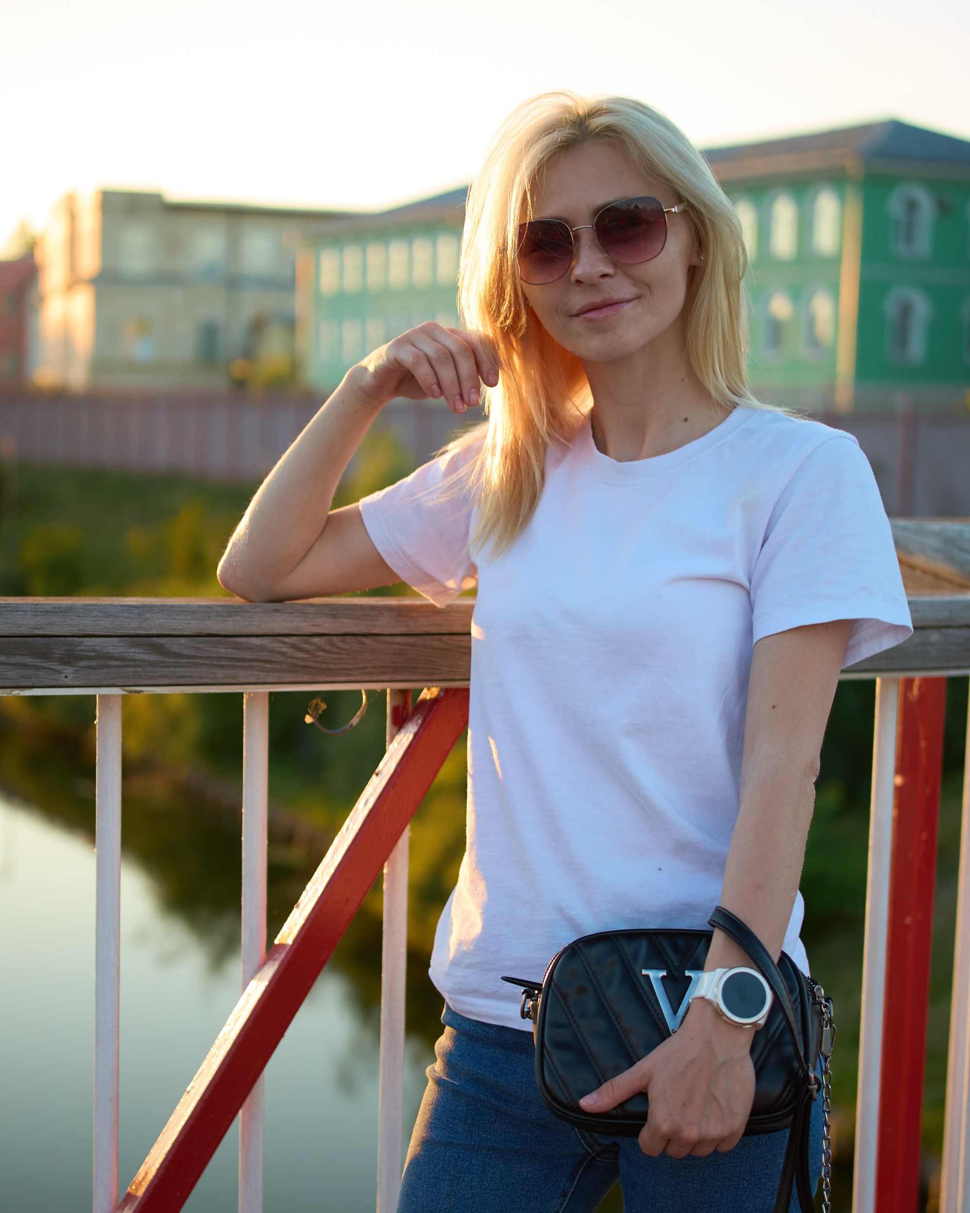 Портрет девушки в профиль в белой футболке и джинсах на фоне реки и городских зданий на закате — фотограф Кураков Максим