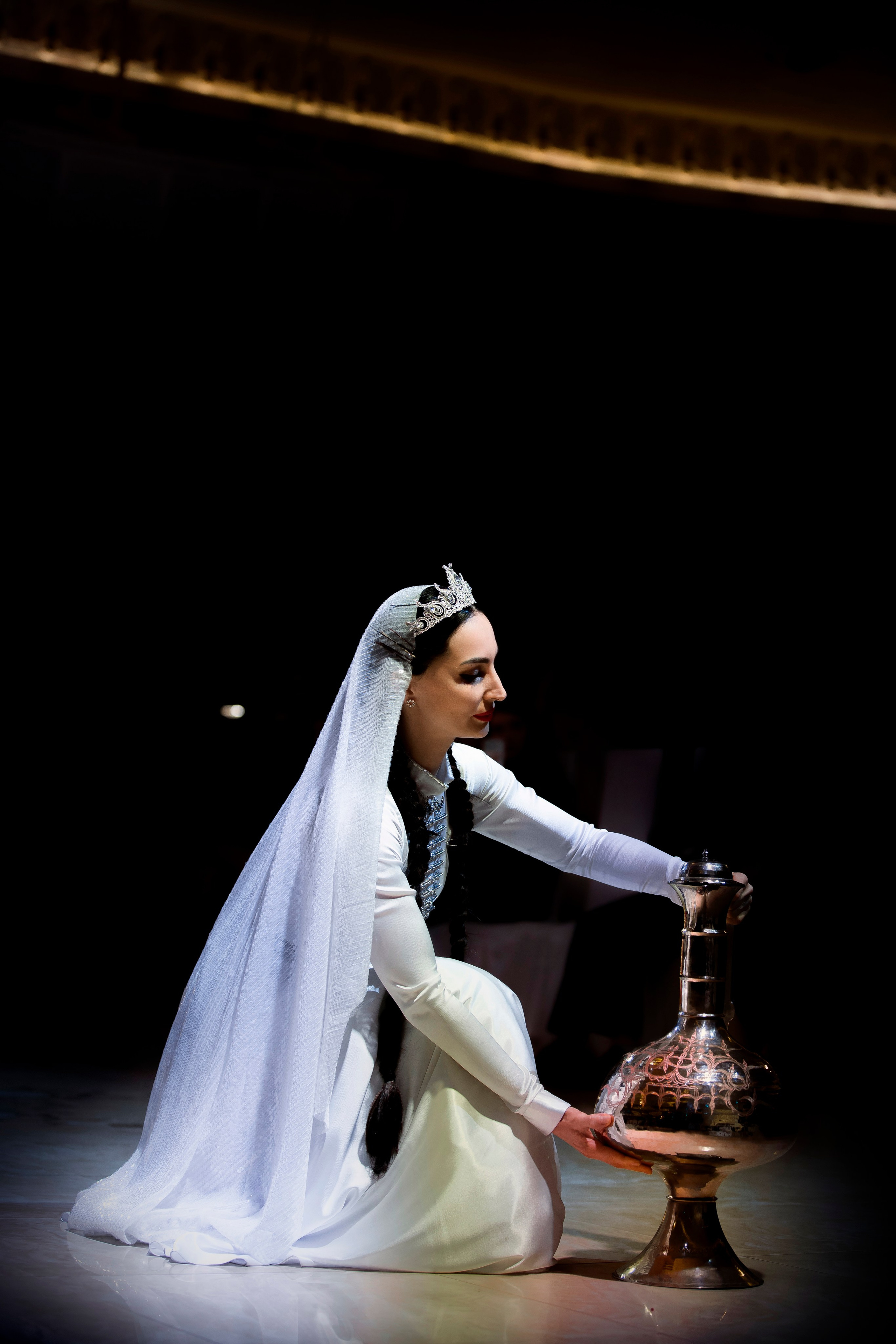 Восточная красавица с лампой Аладдина присела в темноте, золотой софит освещает ее на ED Fashion Show New Names 2024.