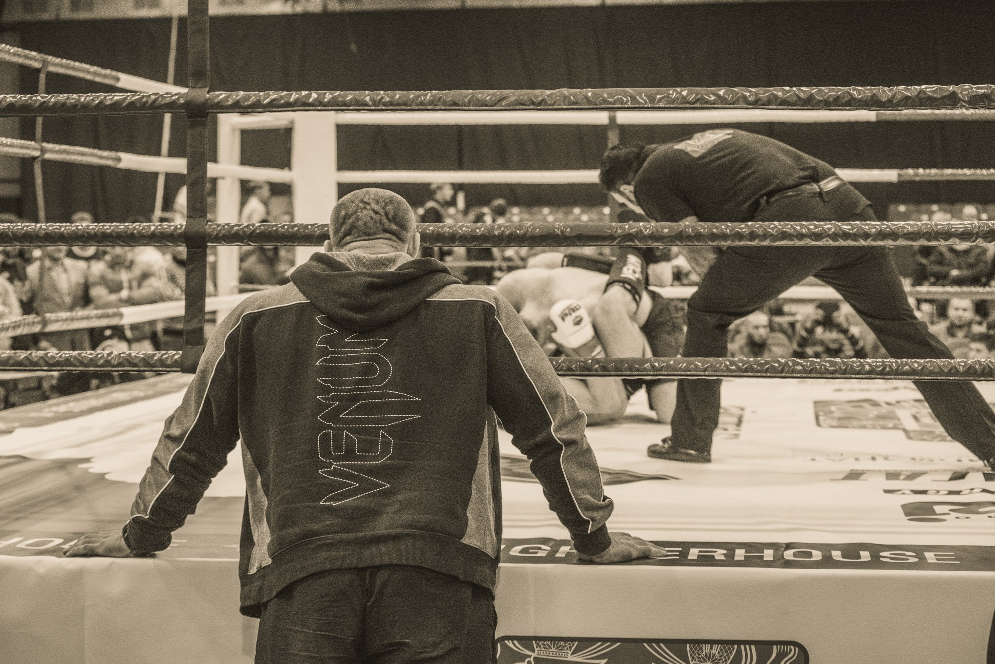 Тренер облокотившись руками на ринг следит за боем своего ученика