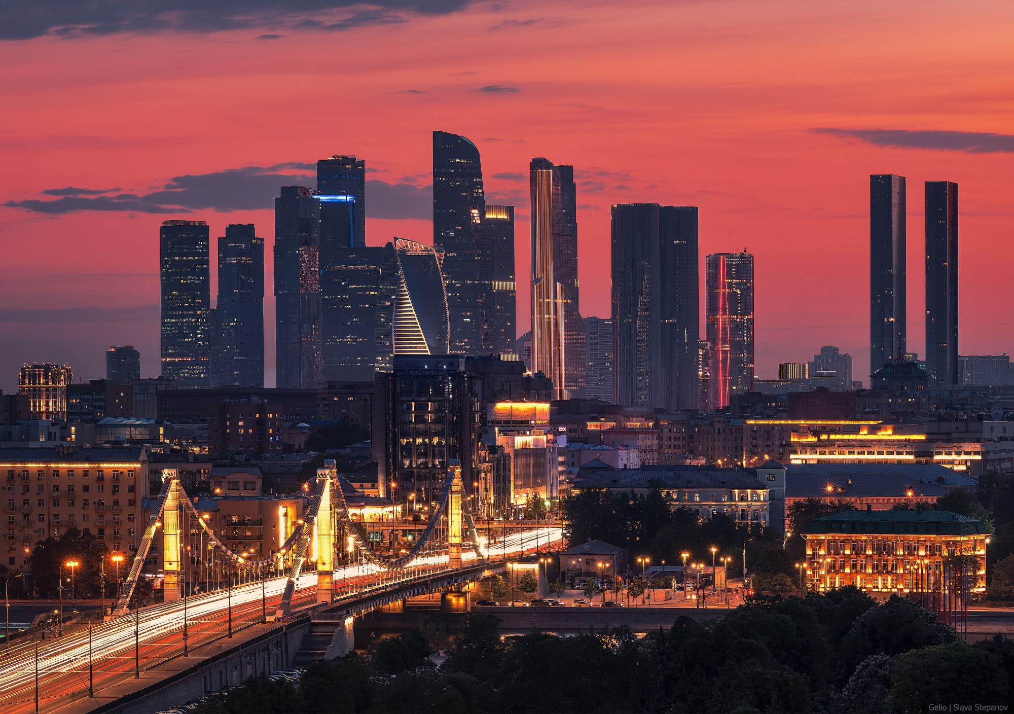 Panorama of evening Moscow against a red sunset. Illuminated Krymsky Bridge with heavy traffic and modern Moscow-City business center skyscrapers on the horizon. Metropolis landscape photography, Gelio.