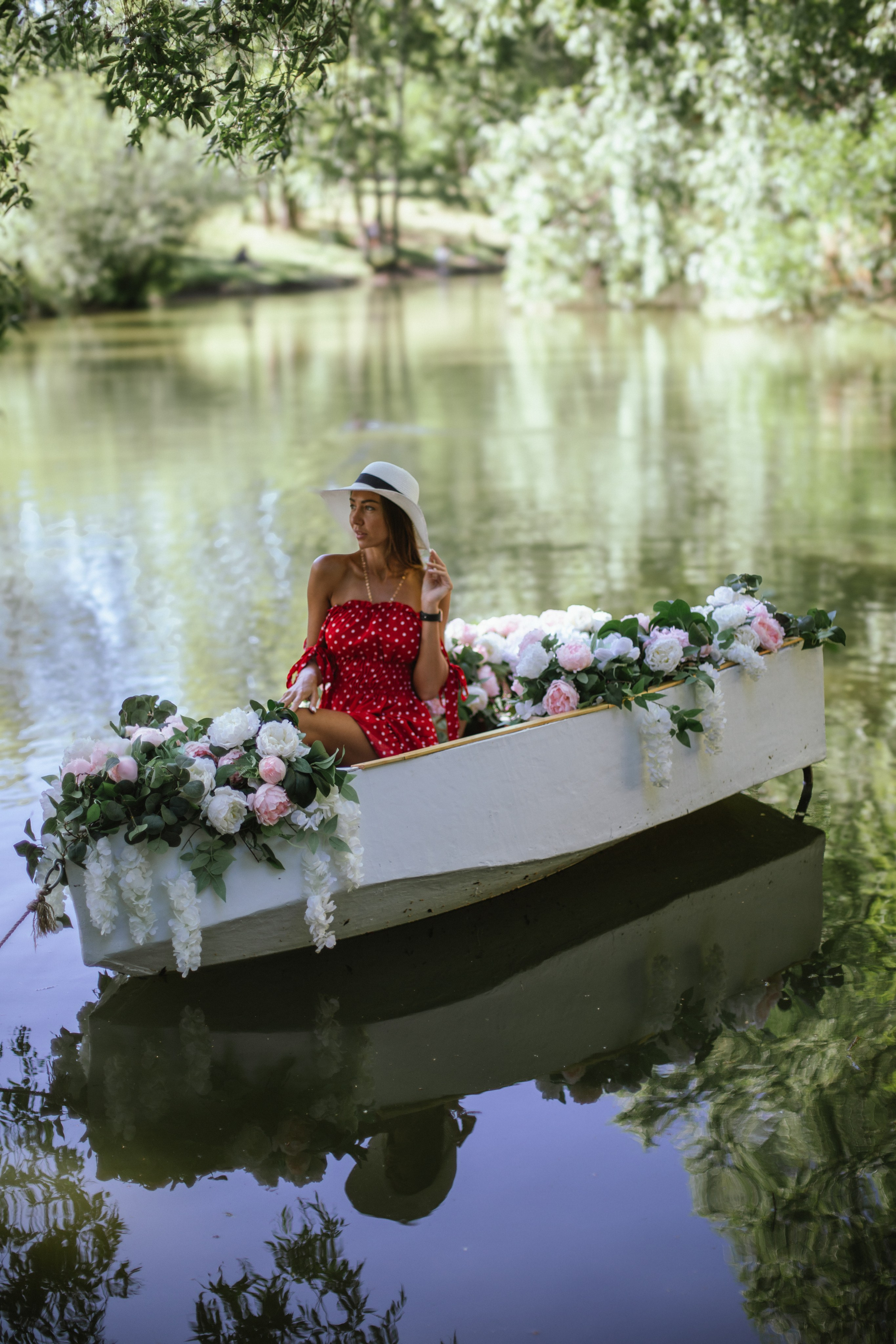 Девушка в красном платье в лодке с цветами на озере