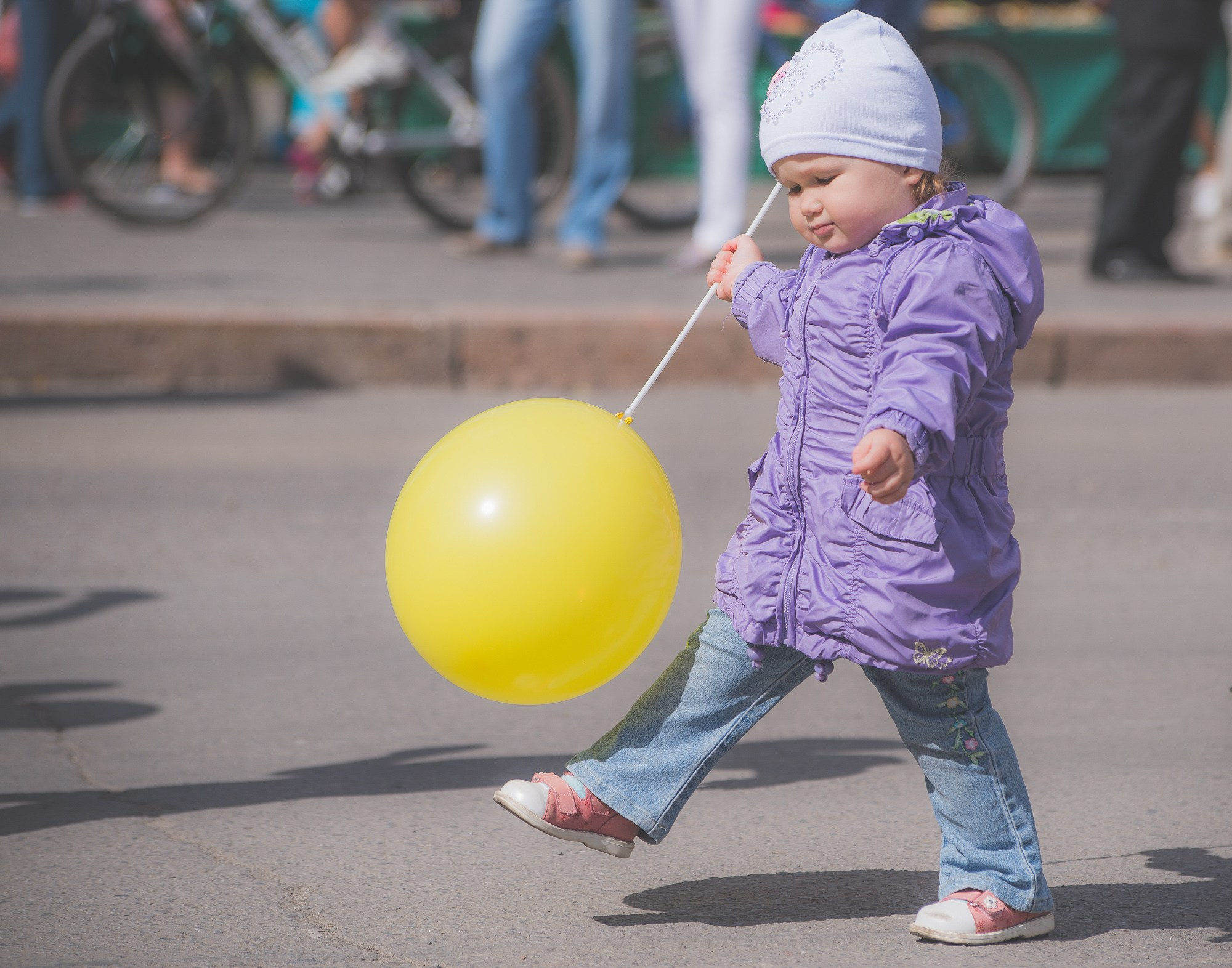 Маленькая девочка в сиреней куртке шагает с жёлтым воздушным шариком