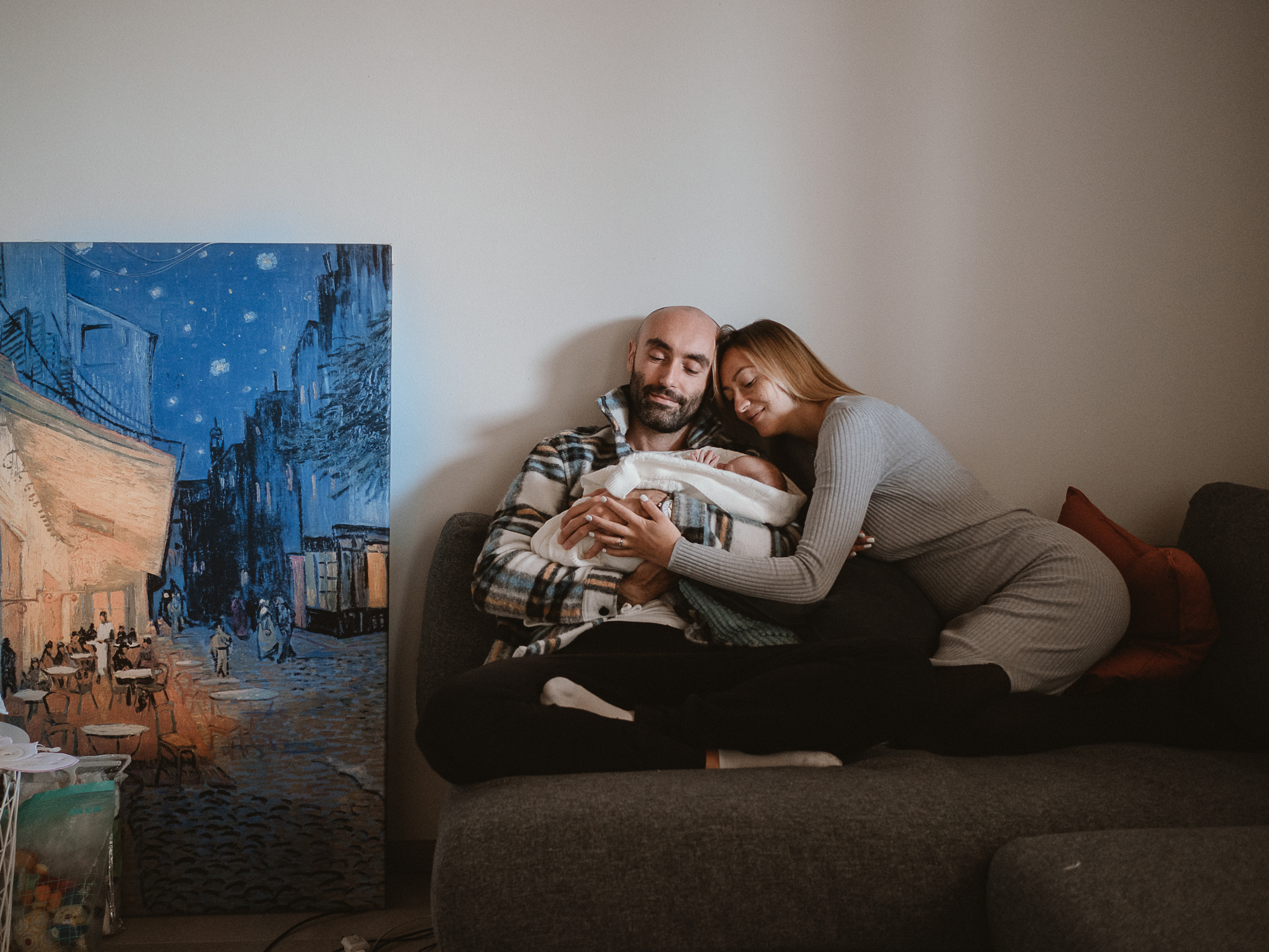 молодая семья сидит на диване с малышом новорожденным на руках