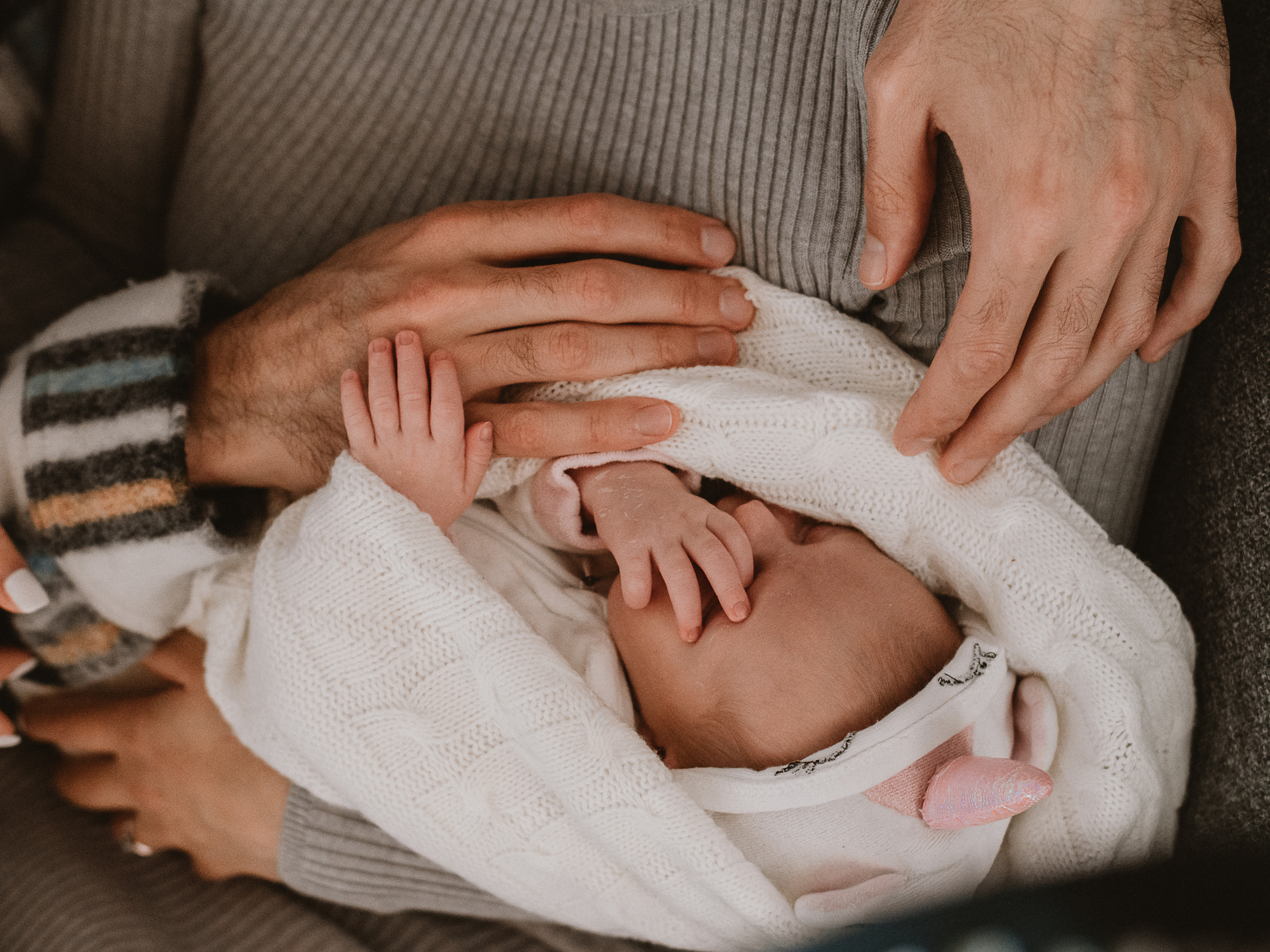 руки родителей и новорожденного малыша обнимают дочку