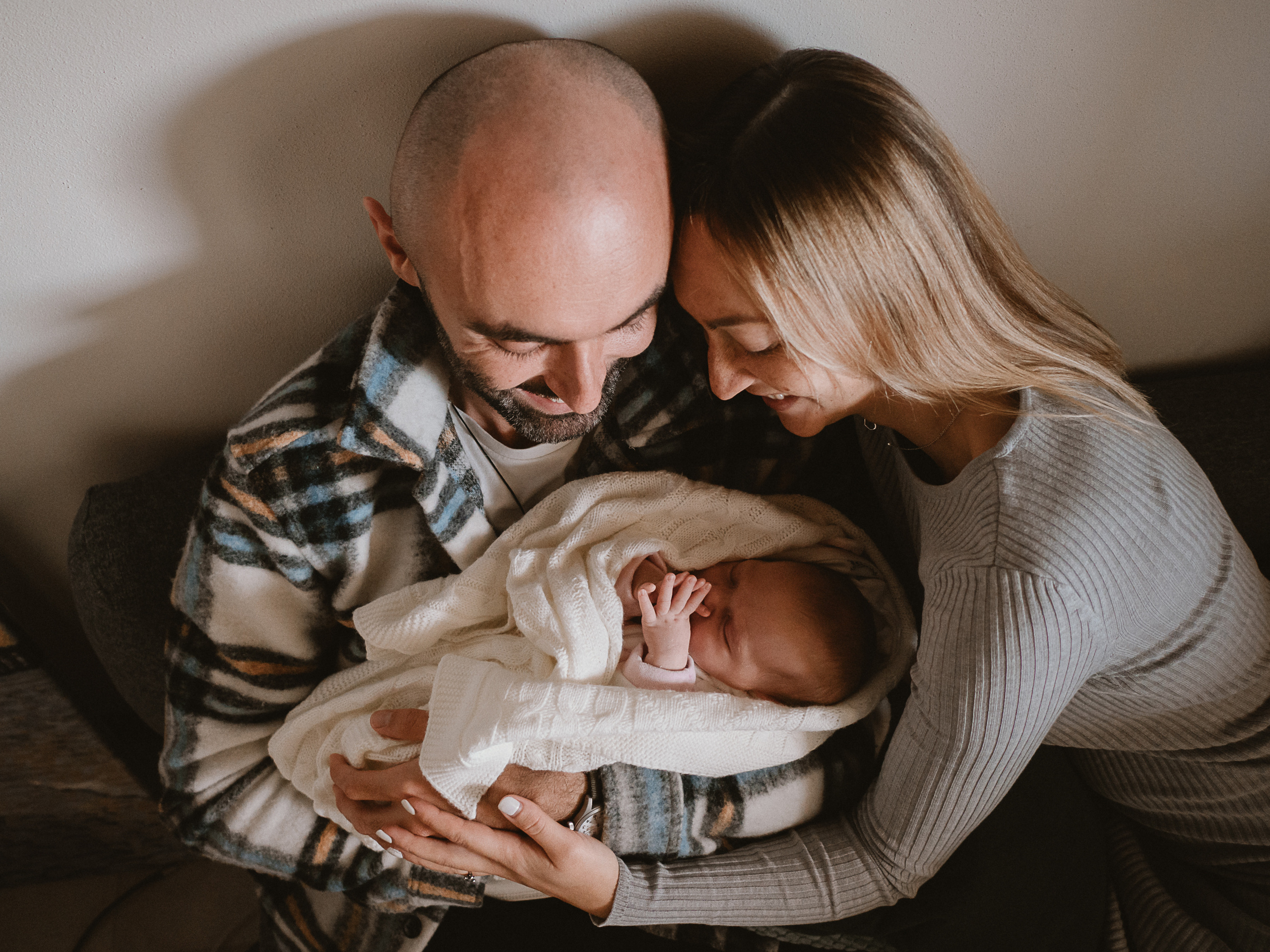 семейная фотосессия малышей молодые родители сидят на диване дома и смотрят на новорожденного малыша