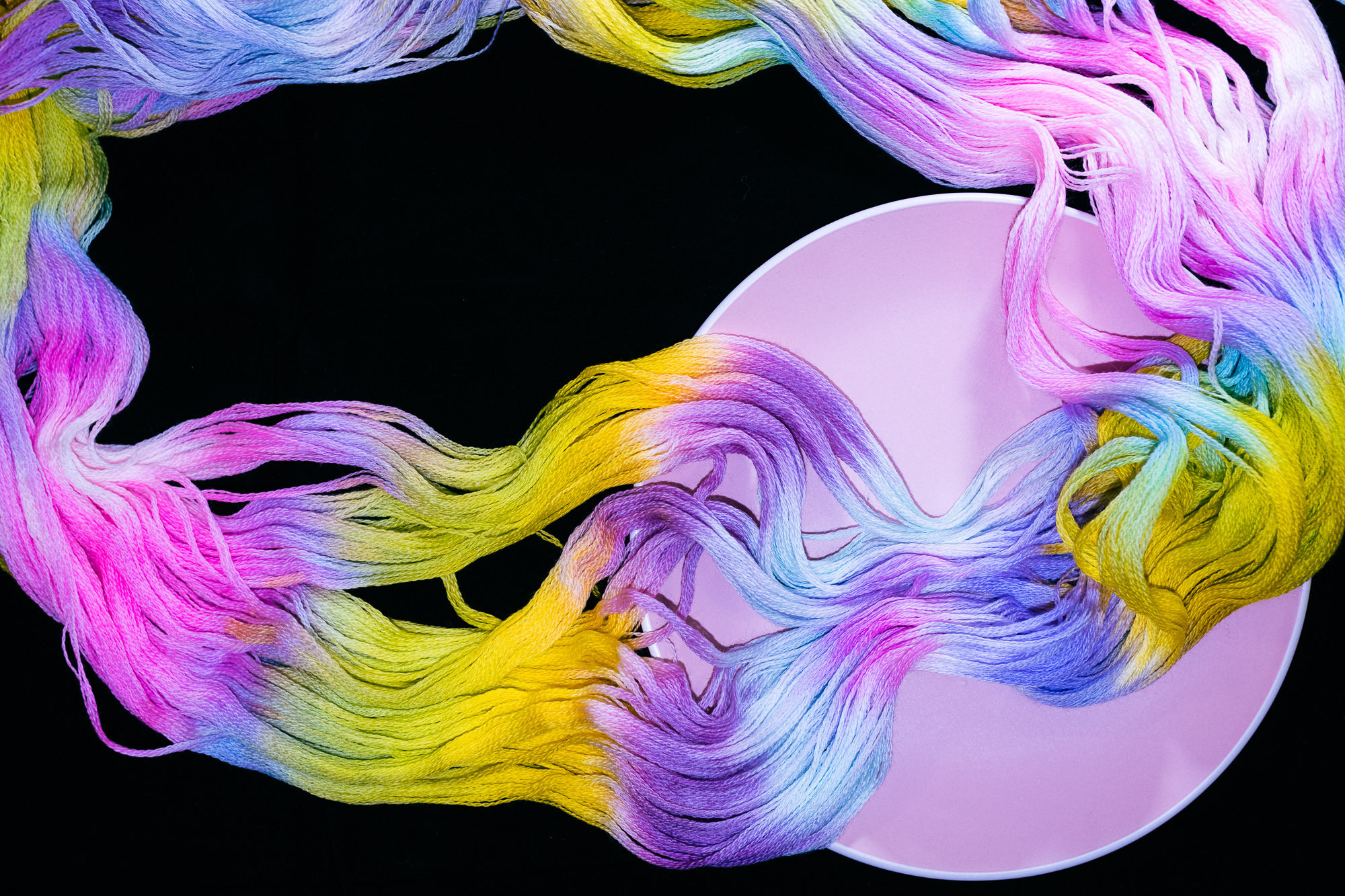 Пряжа как радужная волна на черном фоне и в розовом блюдце
