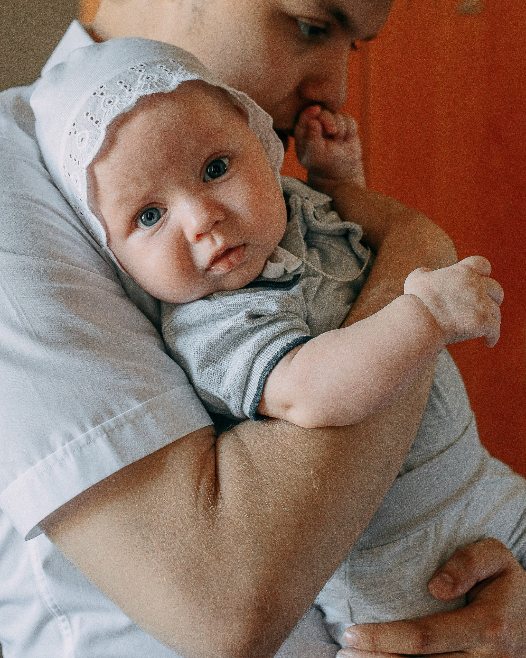 Профессиональная фотосессия крещения в Новосибирске, портрет младенца в крестильной одежде на руках у папы.