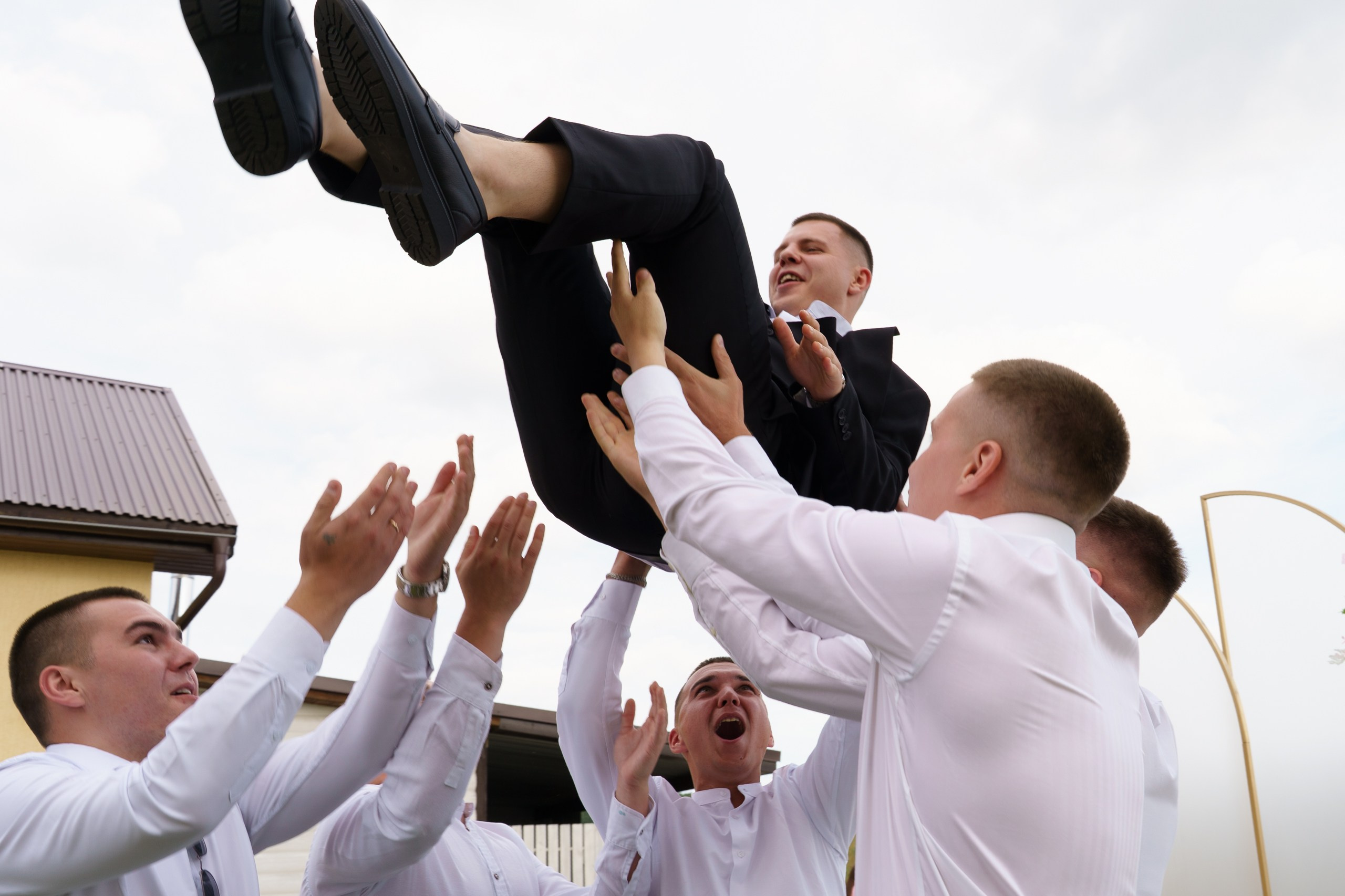 Динамичный кадр со свадьбы: жених взмывает в воздух под весёлые возгласы друзей. Их руки крепко держат его, а лица светятся радостью | свадебный фотограф Екатеринбург