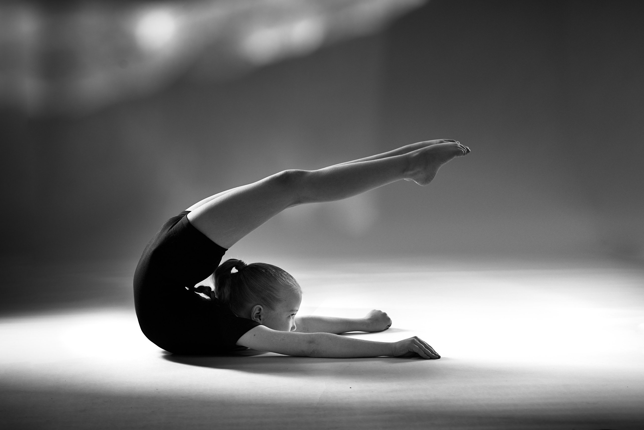 Черно-белое фото юной гимнастки в глубоком прогибе на полу, художественная гибкость и пластика в стиле спортарт