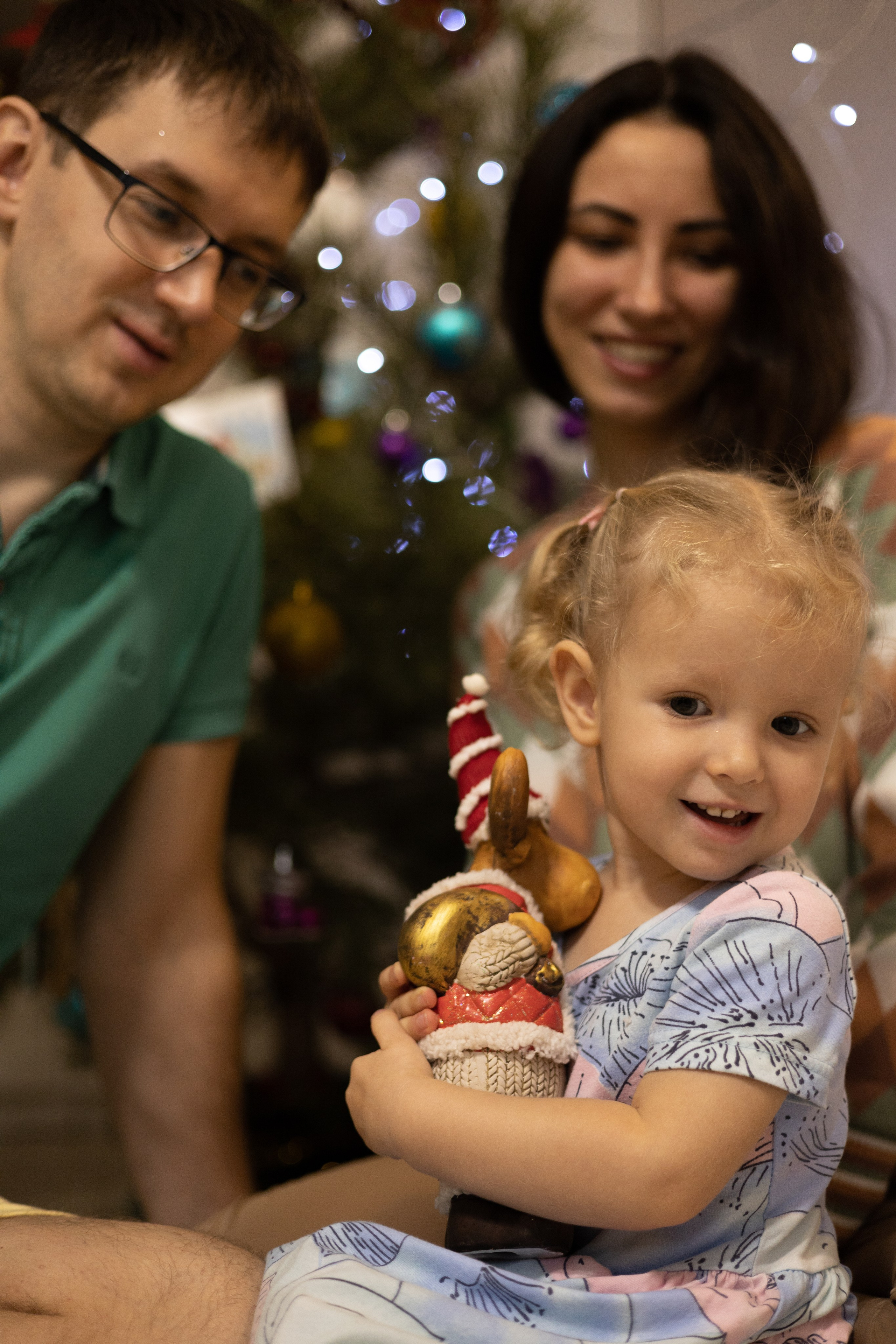 Девочка радуется новогоднему подарку рядом с мамой и папой