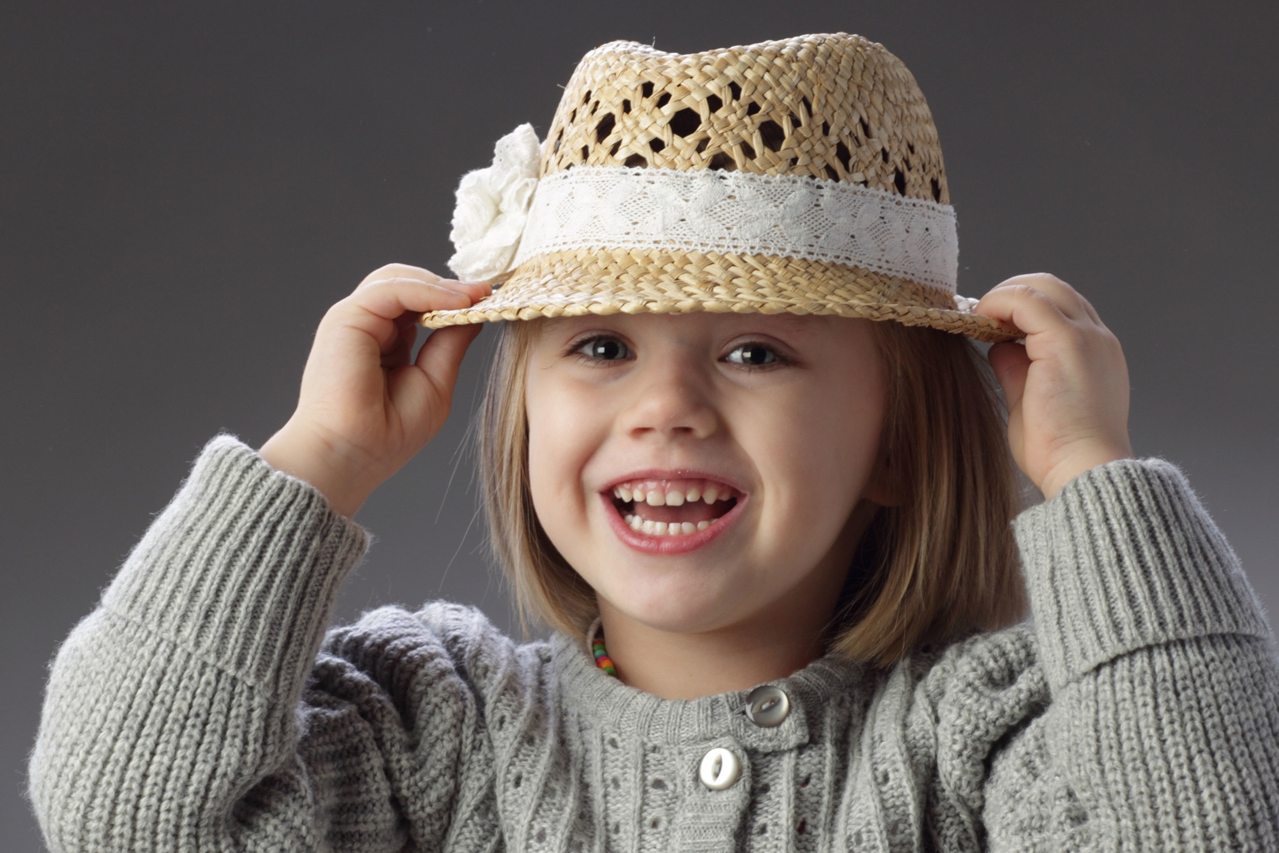 озорная девочка с улыбкой  примеряет соломенную шляпку.