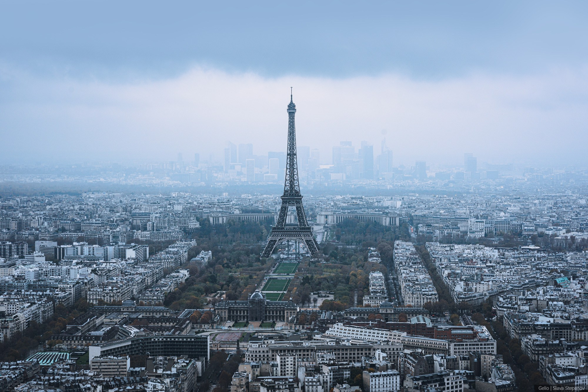 Elevated panorama of Paris in overcast weather. The Eiffel Tower stands against the modern skyscrapers of the La Défense business district. "Cities of the World" project, photographer Gelio.