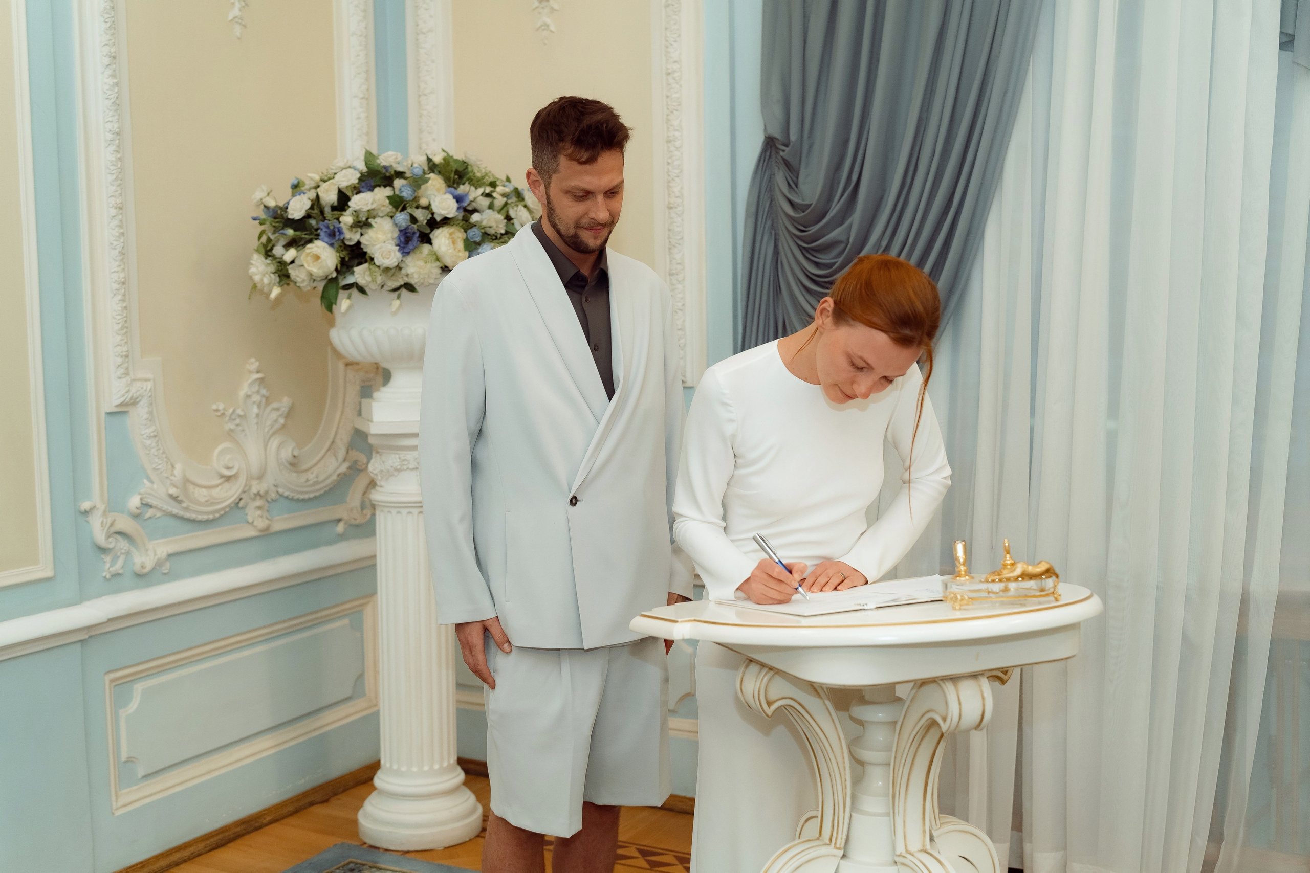 Мария подписывает акт о браке на изящном столике с позолоченным пером в голубом зале