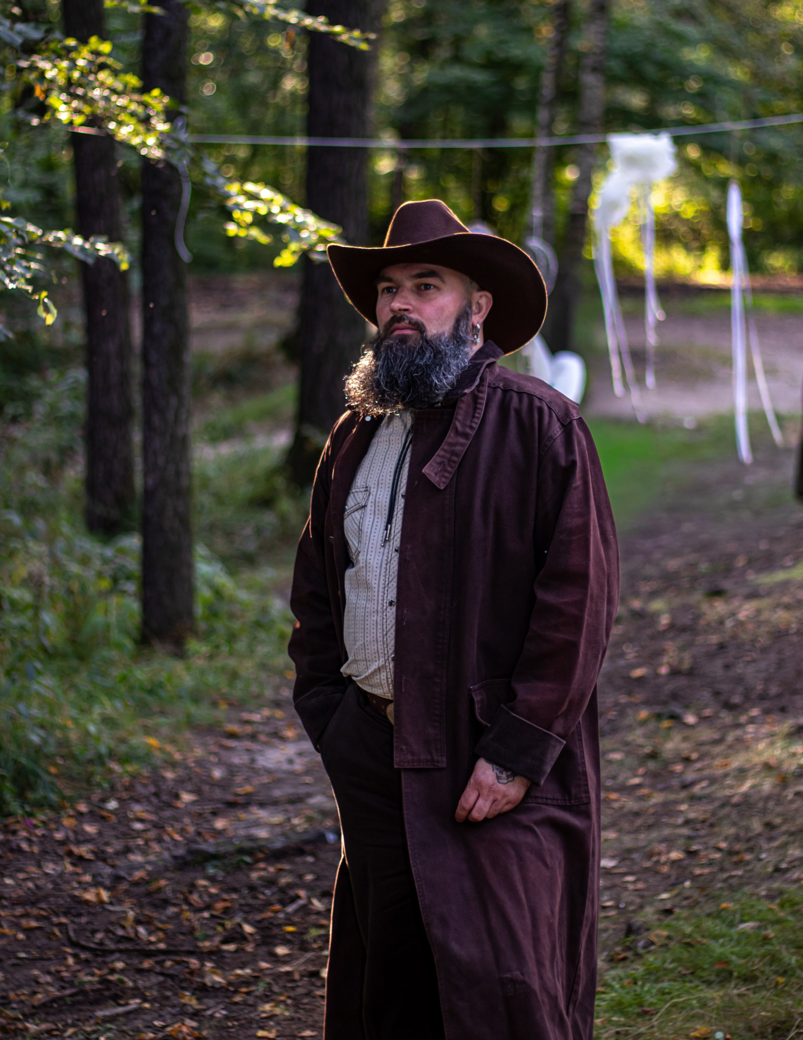 Мужчина в длинном пальто идёт по лесной тропинке