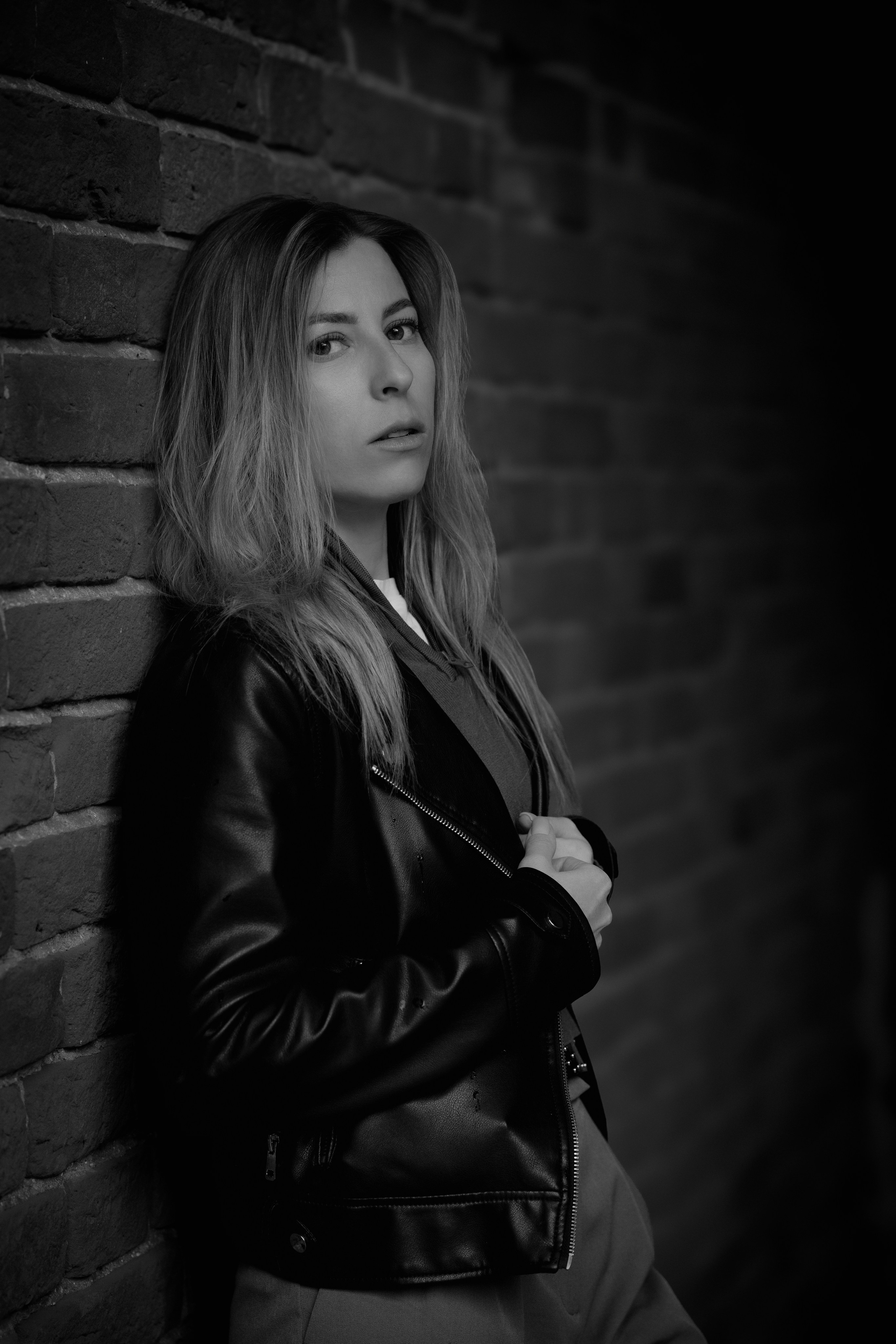 Черно-белая фотография девушки в кожаной куртке на фоне кирпичной стены
