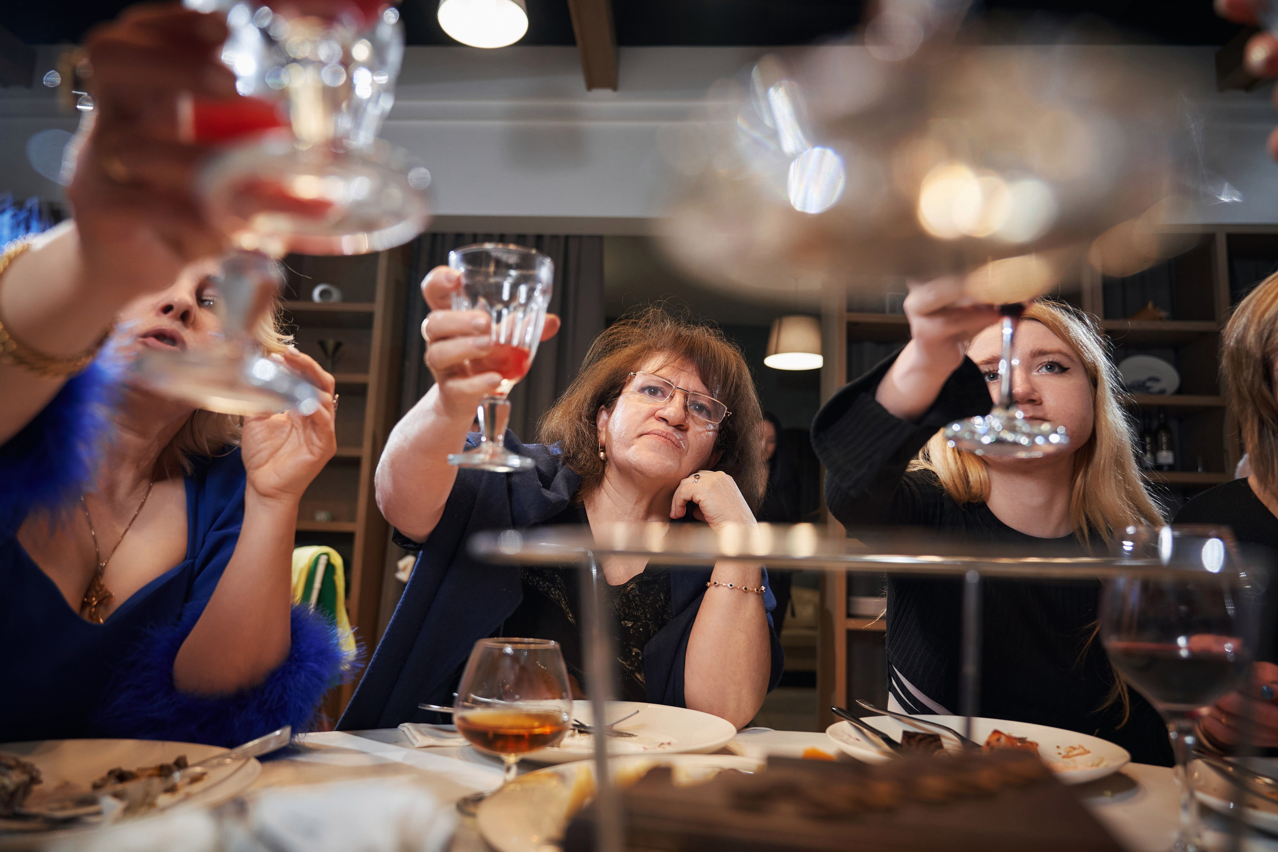 девушки за праздничным столом чокаются бокалами со спиртными напитками