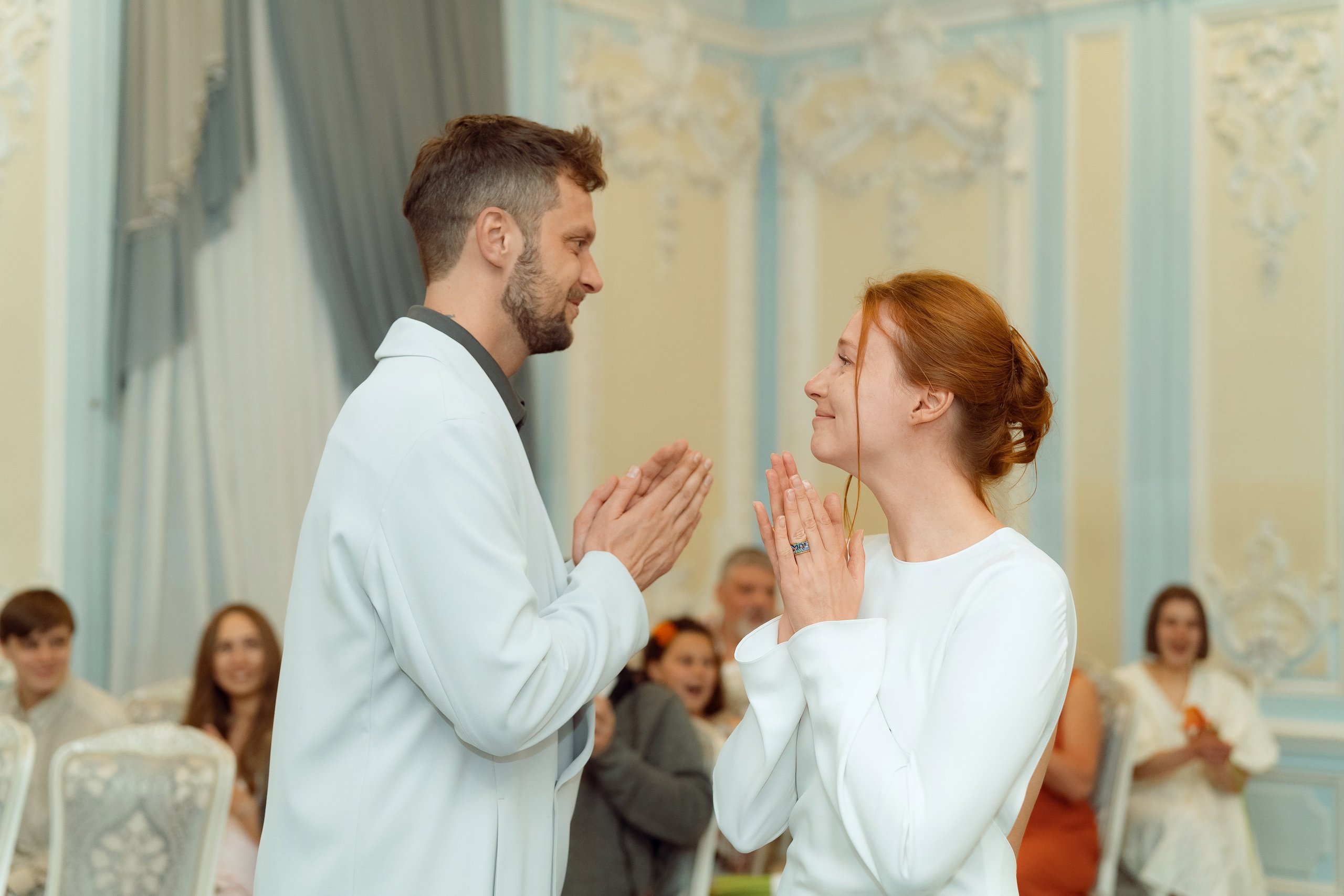 Евгений показывает кольцо Марии, пара смеётся, голубые стены зала с лепниной позади