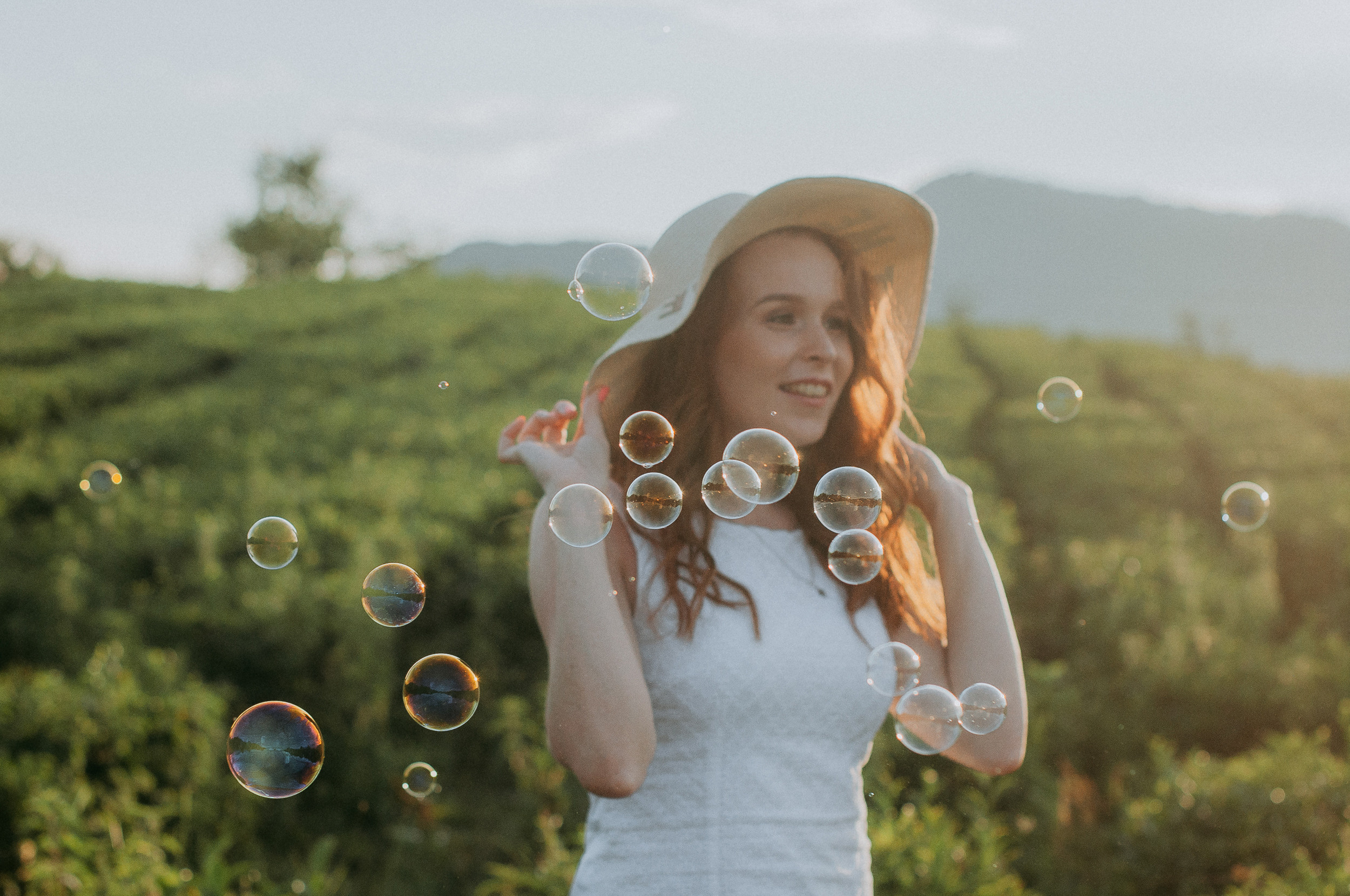 Рыжая девушка в шляпе в окружении мыльных пузырей на закате на чайных плантациях Мацеста