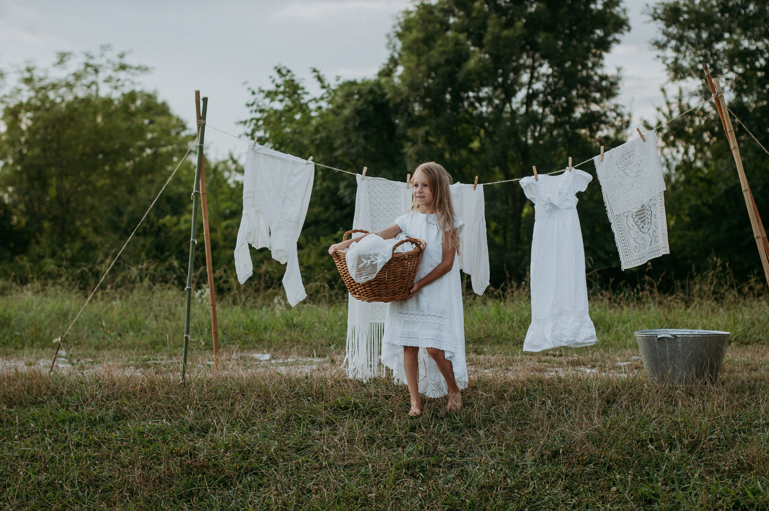 Девочка держит в руках корзину с бельем, на фоне развешенное на сушилке белье