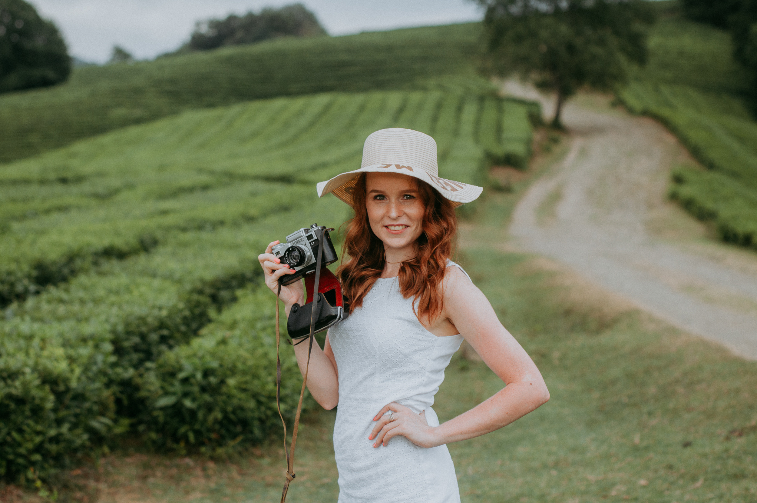 Рыжая девушка в шляпе с ретро фотоаппаратом на фотосессии на чайной плантации в Сочи