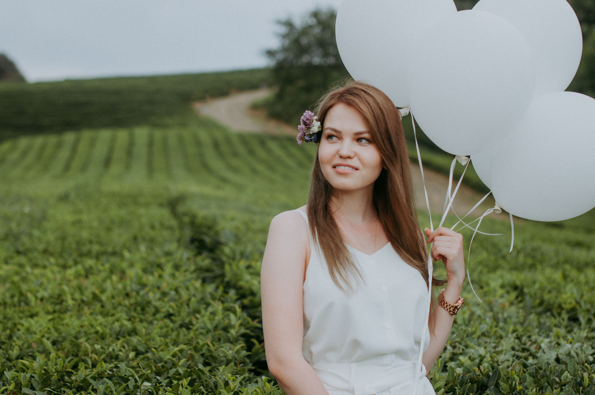 Красивая шатенка в белом с белыми воздушными шарами на чайных плантациях в Сочи