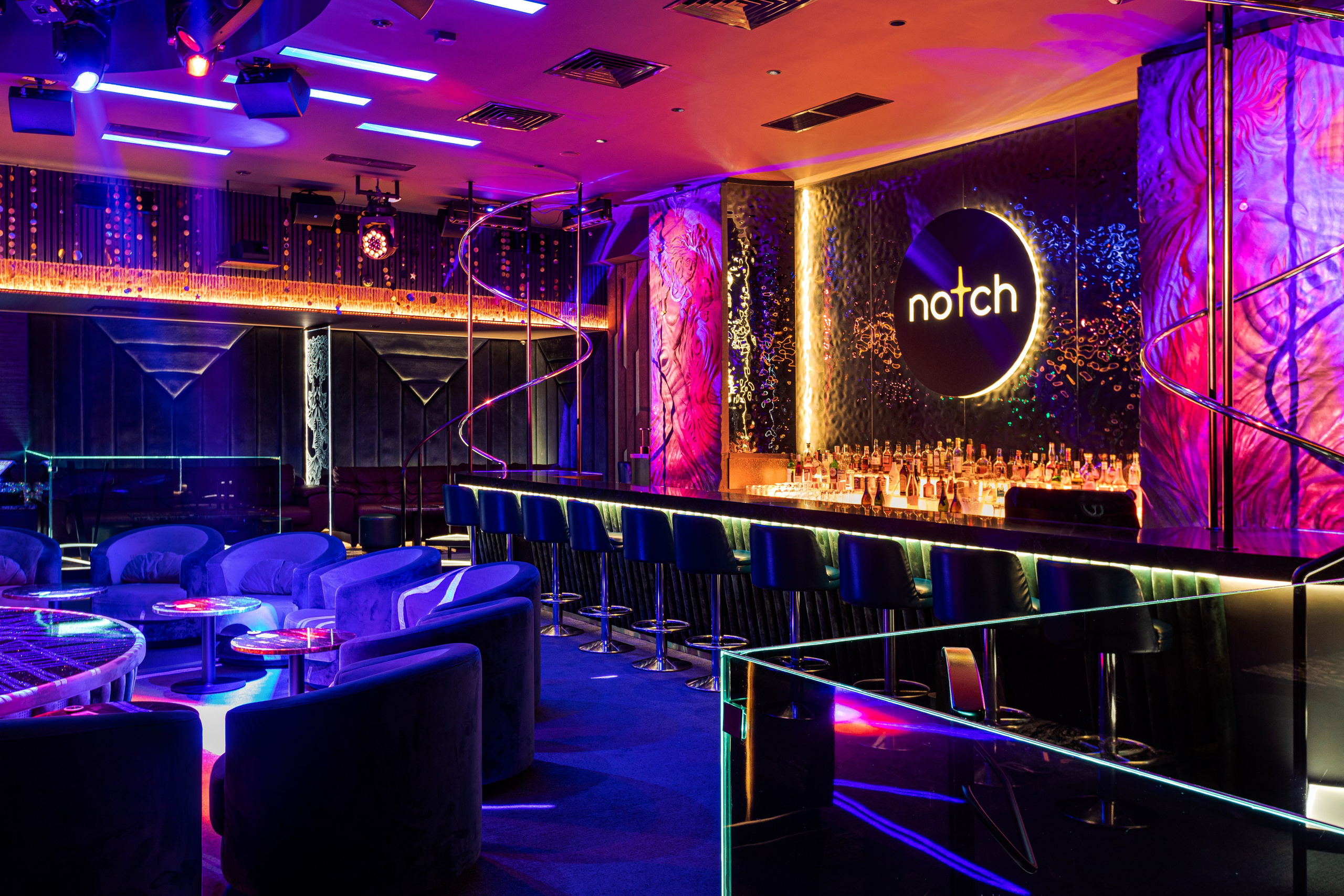 Интерьерная съёмка для стрип-клуба NOTCH: стильный современный зал с барной стойкой, мягкими креслами и атмосферным неоновым освещением в фиолетово-синих тонах. На стене за баром светится логотип клуба, создавая акцент в композиции кадра