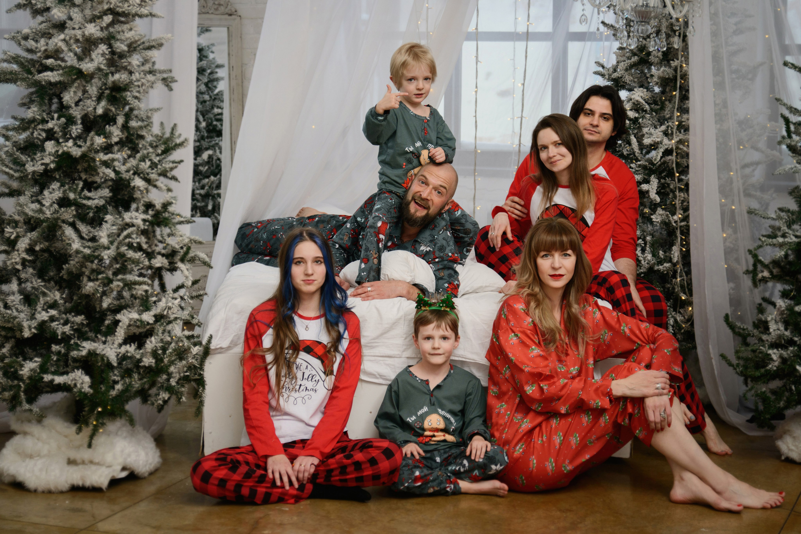 Мама, папа, взрослый сын с невестой и средняя дочка позируют в новогоднем интерьере в спальне