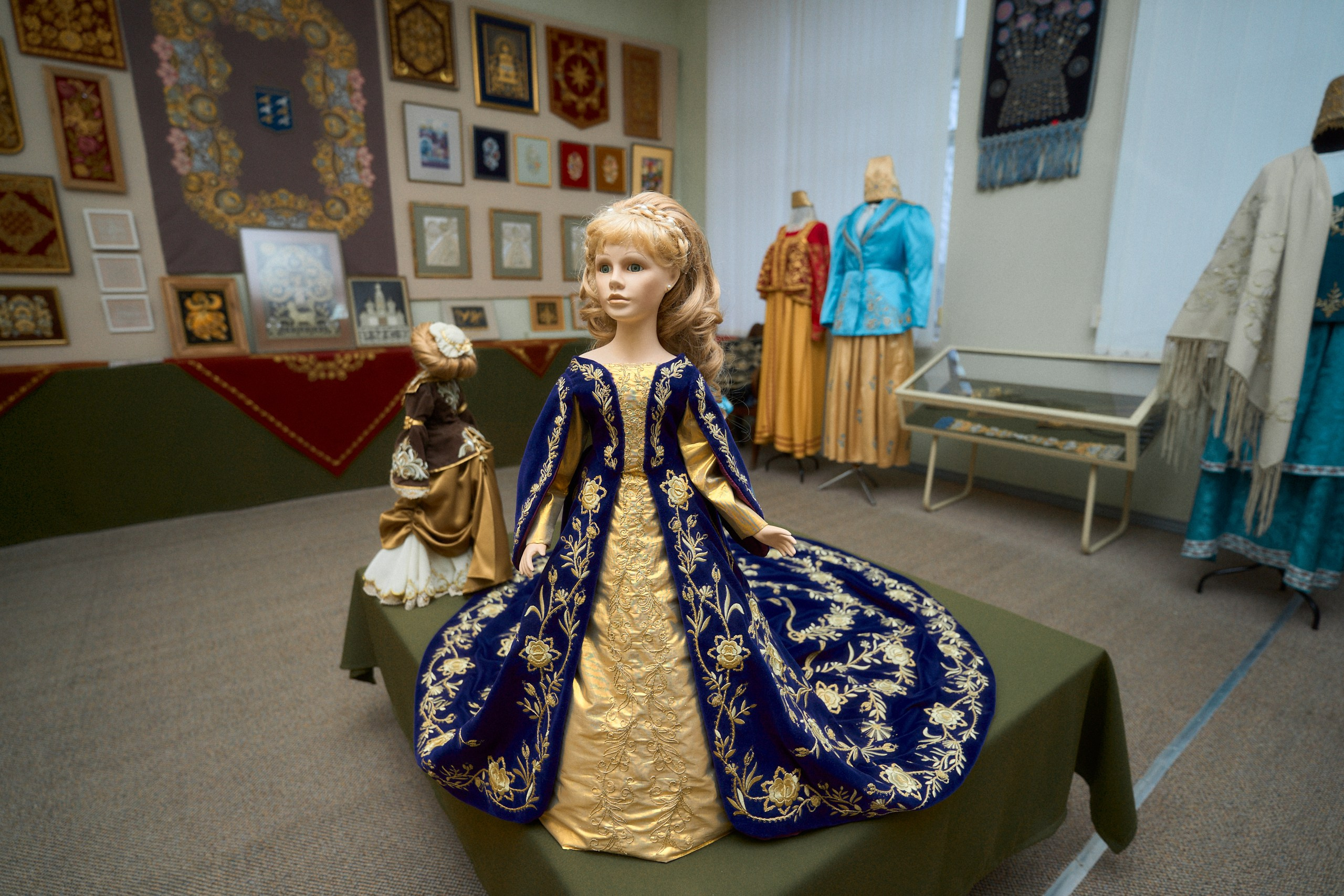 Выставка в Музее торжокских золотошвей в Торжке, демонстрирующая манекены в традиционных русских нарядах с золотой вышивкой и сложными узорами, на фоне стен, украшенных картинами и орнаментами